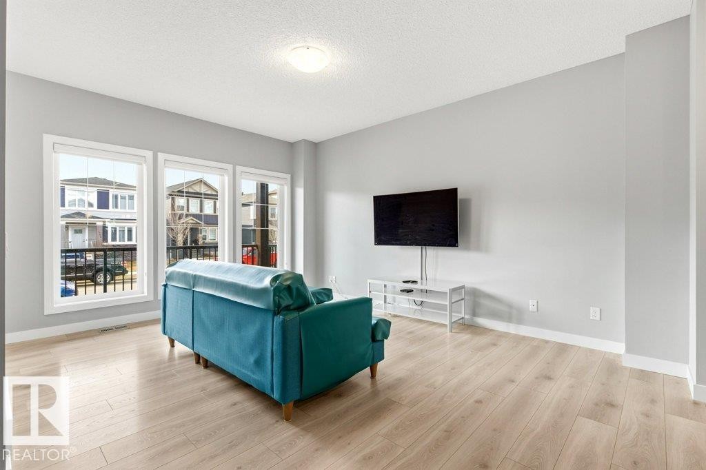 Bright living area featuring wood-finish flooring, light gray walls, white baseboards, and a series of three large windows - 17451 77 Street, Edmonton, AB - Indoor Photo Showing Living Room