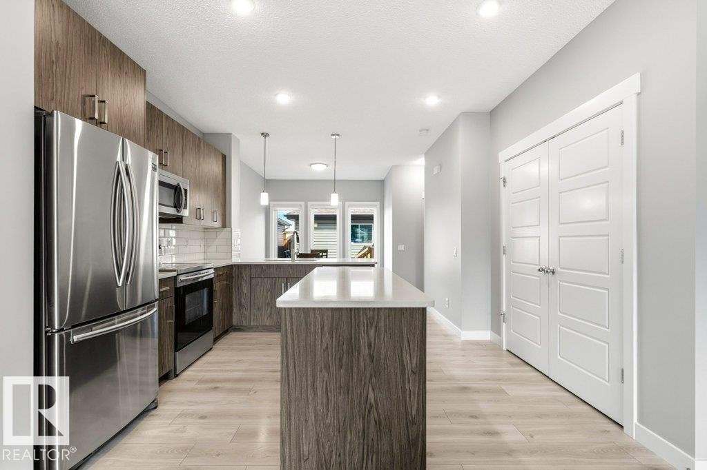 Modern kitchen featuring stainless steel appliances, wood-finish cabinetry, a subway tile backsplash, and light wood-finish flooring - 17451 77 Street, Edmonton, AB - Indoor Photo Showing Kitchen With Upgraded Kitchen
