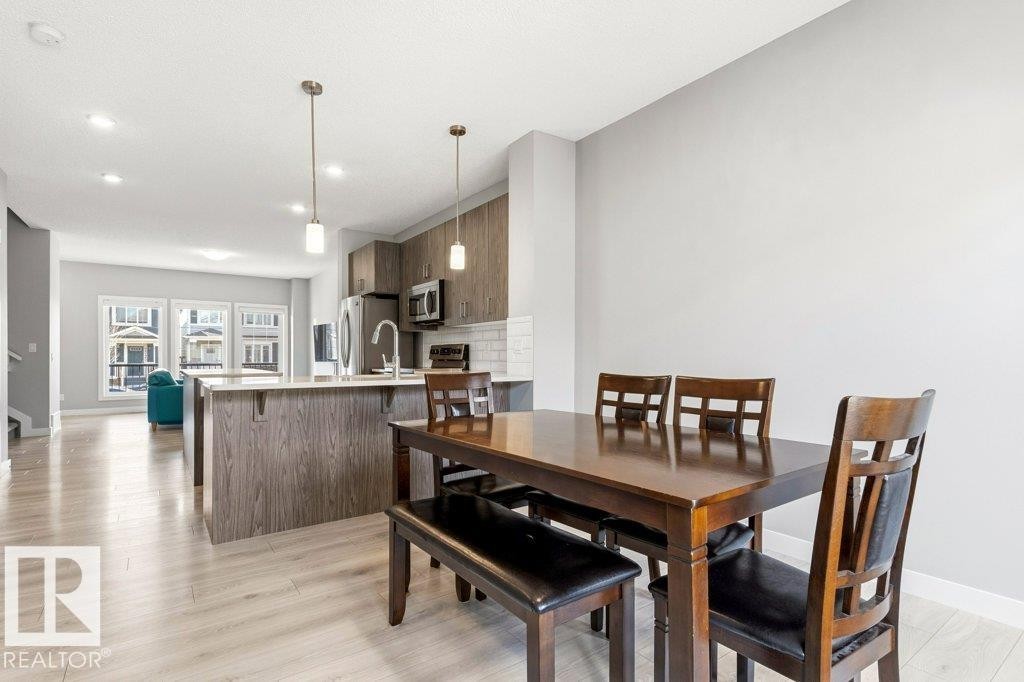 Open-concept dining and kitchen area featuring light wood-finish flooring, a kitchen island with seating, pendant lighting, and stainless steel appliances - 17451 77 Street, Edmonton, AB - Indoor