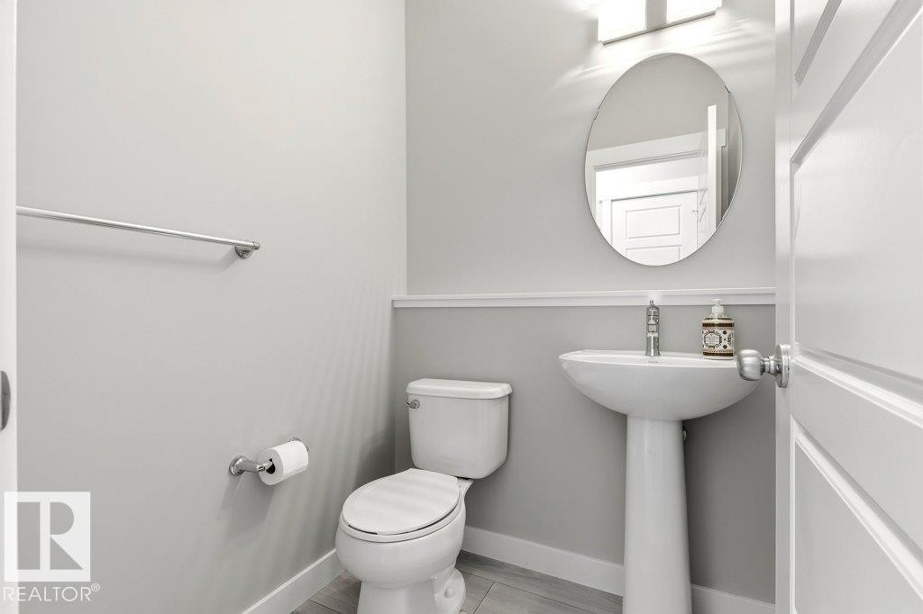 Pedestal sink with chrome faucet, oval mirror, and wall-mounted light fixture - 17451 77 Street, Edmonton, AB - Indoor Photo Showing Bathroom
