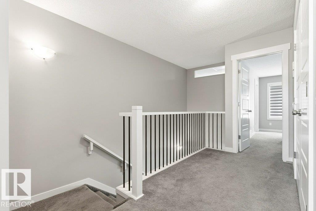 Carpeted upper landing featuring a contemporary railing with white posts and black balusters, a rectangular transom window, and a wall-mounted light fixture - 17451 77 Street, Edmonton, AB - Indoor Photo Showing Other Room