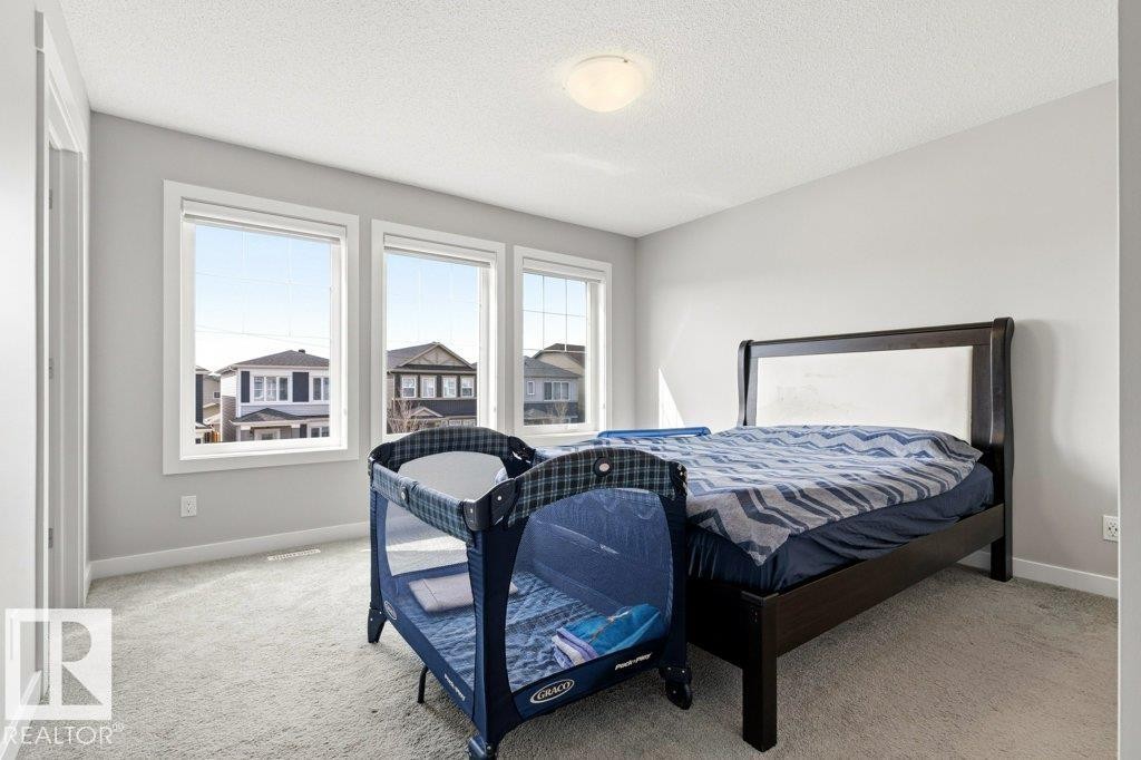 Bright room featuring three large windows, light gray wall paint, textured ceiling, light-toned carpet flooring, and white trim - 17451 77 Street, Edmonton, AB - Indoor Photo Showing Bedroom
