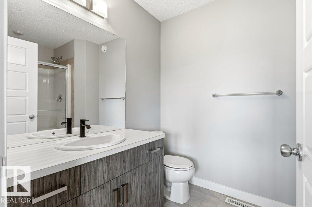 Bathroom featuring a wood-grain vanity with a white countertop and integrated sink, matte black faucet, and a large mirror - 17451 77 Street, Edmonton, AB - Indoor Photo Showing Bathroom