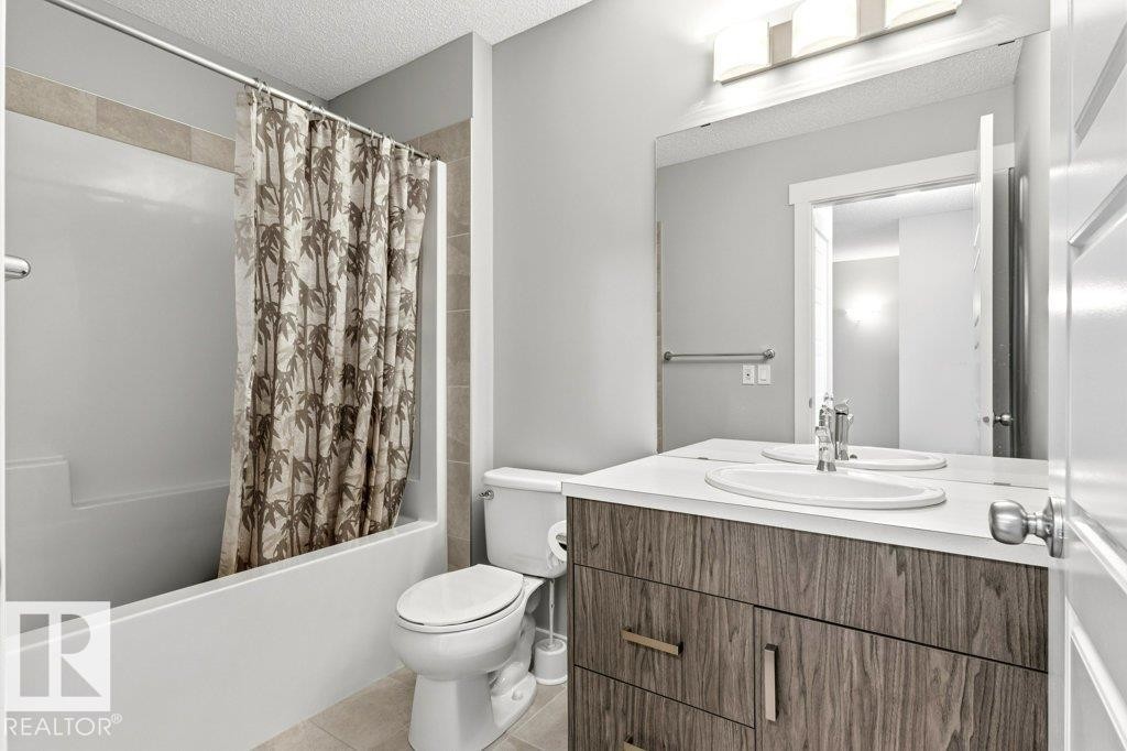 Bathroom featuring a built-in tub with tile surround, wood-finish vanity with an integrated sink, polished chrome faucet, and overhead lighting fixture - 17451 77 Street, Edmonton, AB - Indoor Photo Showing Bathroom