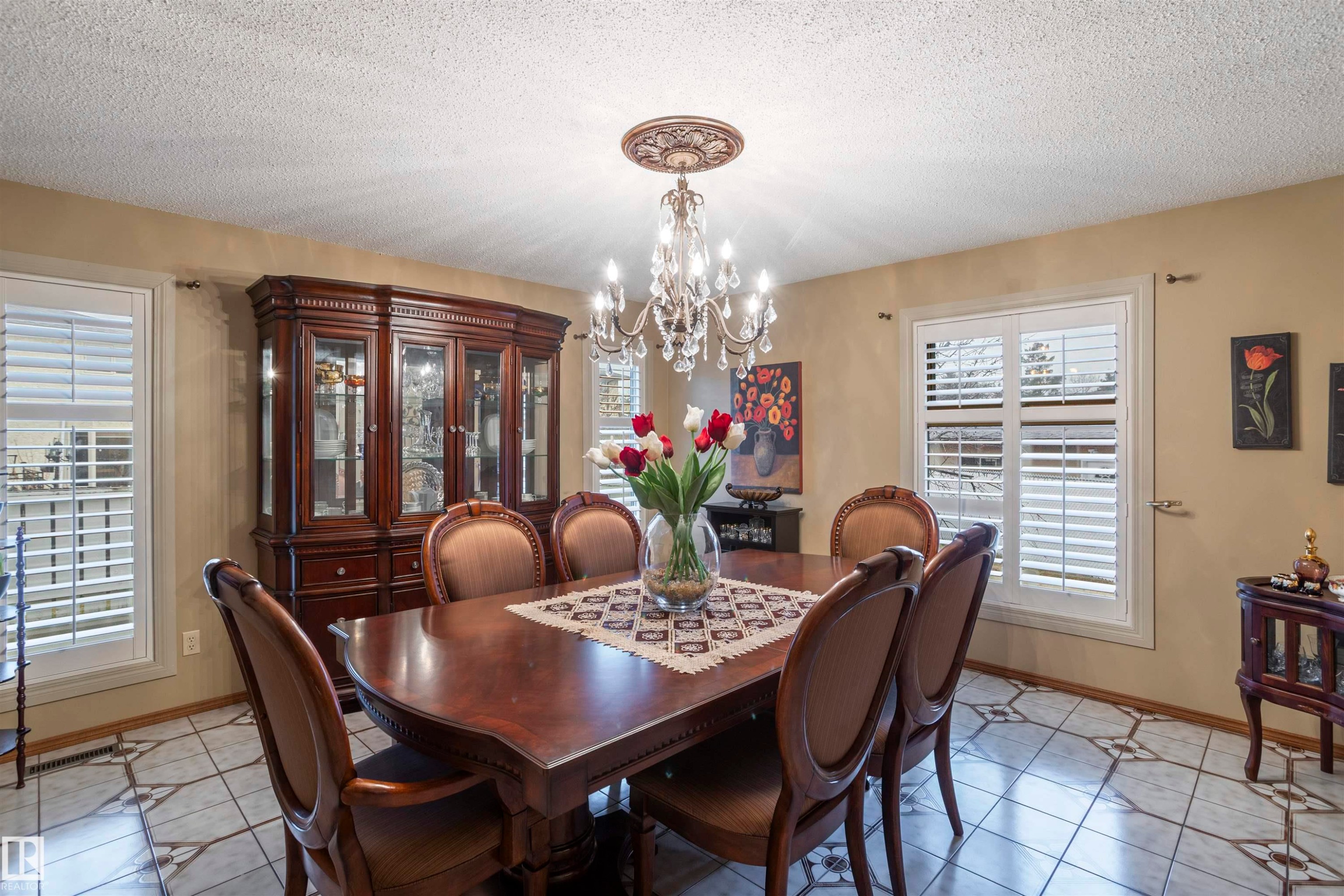 Dining area featuring a crystal chandelier with a decorative ceiling medallion, patterned tile flooring, and multiple windows with white plantation shutters - 9831 158 Avenue, Edmonton, AB - Indoor Photo Showing Dining Room