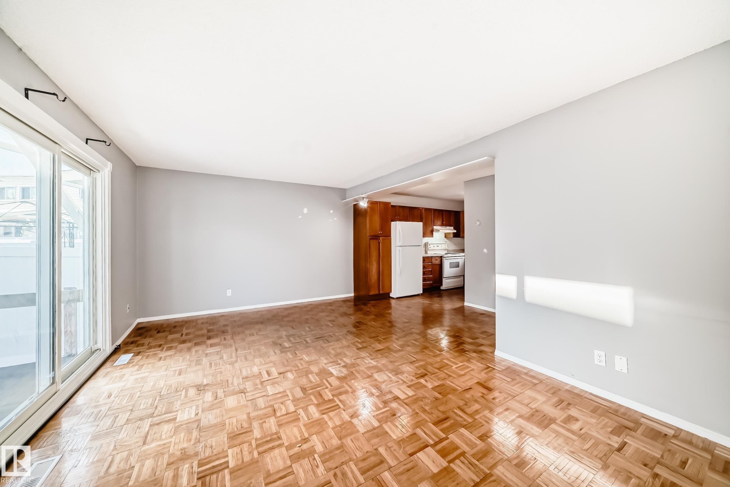 The property features parquet flooring and light gray walls, with sliding glass doors providing access to the outside - 8217 182 Street Nw, Edmonton, AB - Indoor Photo Showing Other Room