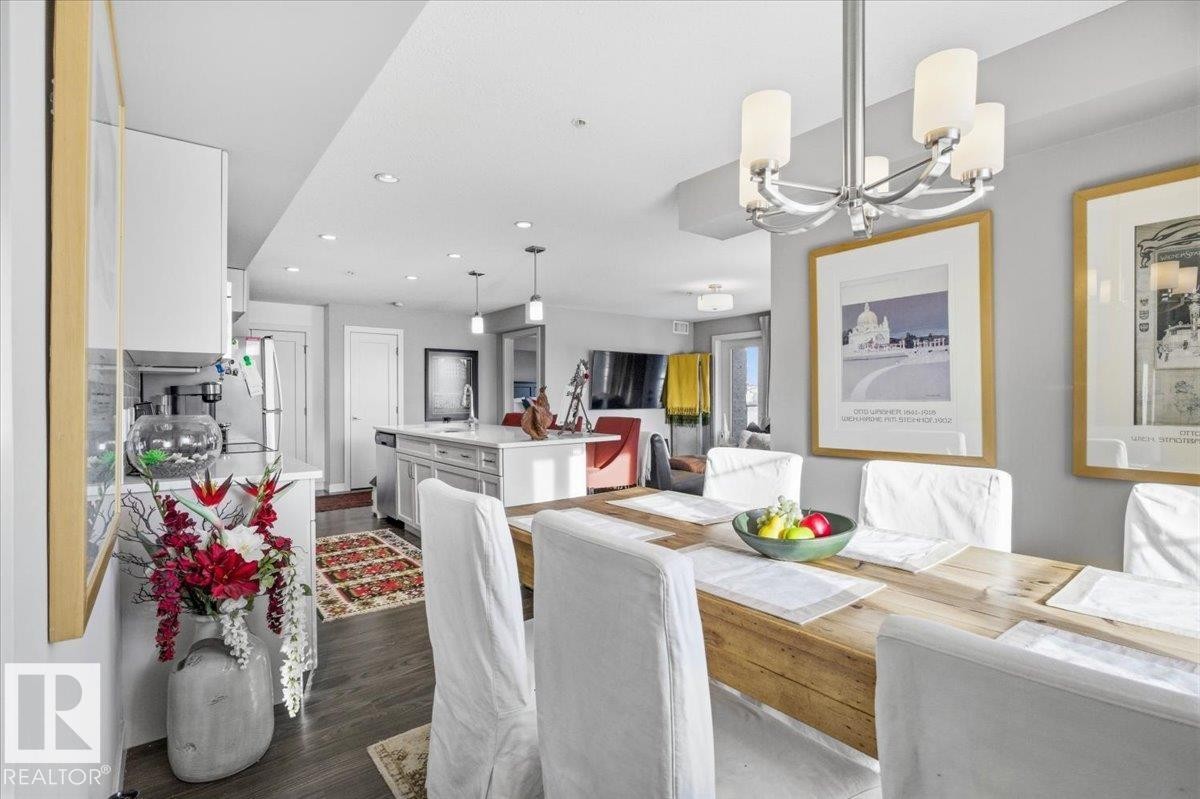 The dining area features a wooden table with white chairs, illuminated by a modern chandelier - 211 5029 Edgemont Boulevard, Edmonton, AB - Indoor Photo Showing Dining Room