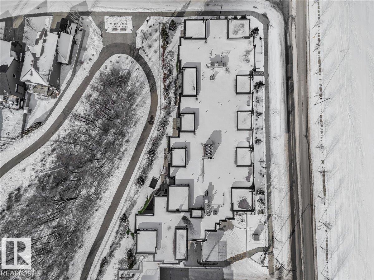 Aerial view of the property and its surrounding area, featuring a paved road, a winding pathway, and rows of structures with snowy rooftops - 211 5029 Edgemont Boulevard, Edmonton, AB -