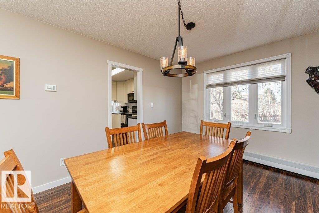 Dining area featuring a contemporary chandelier, large window with blinds, and wood-finish flooring - 1727 65 Street, Edmonton, AB - Indoor Photo Showing Dining Room