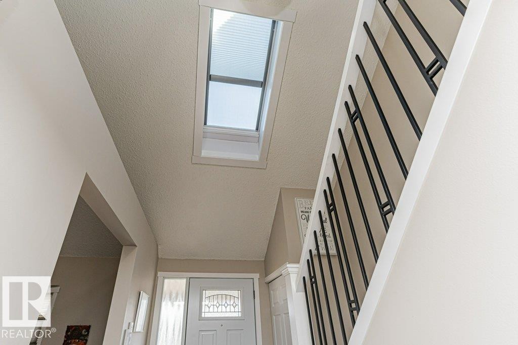 Entryway featuring a skylight with integrated blind, a white front door with decorative glass inserts, and a staircase with black metal balusters - 1727 65 Street, Edmonton, AB - Indoor Photo Showing Other Room