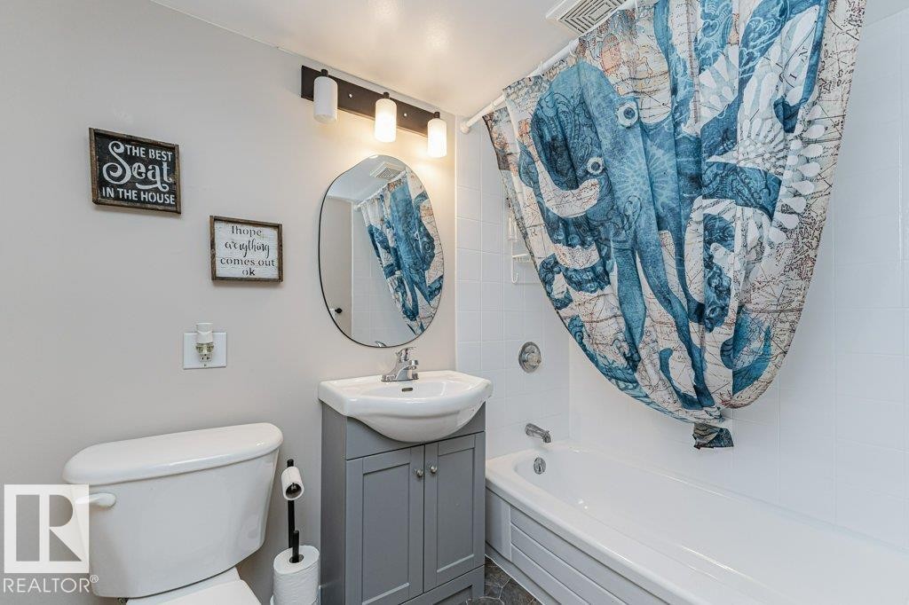 Bathroom featuring a white bathtub with subway tile surround, gray vanity with integrated sink, oval mirror, and a three-light fixture - 1727 65 Street, Edmonton, AB - Indoor Photo Showing Bathroom