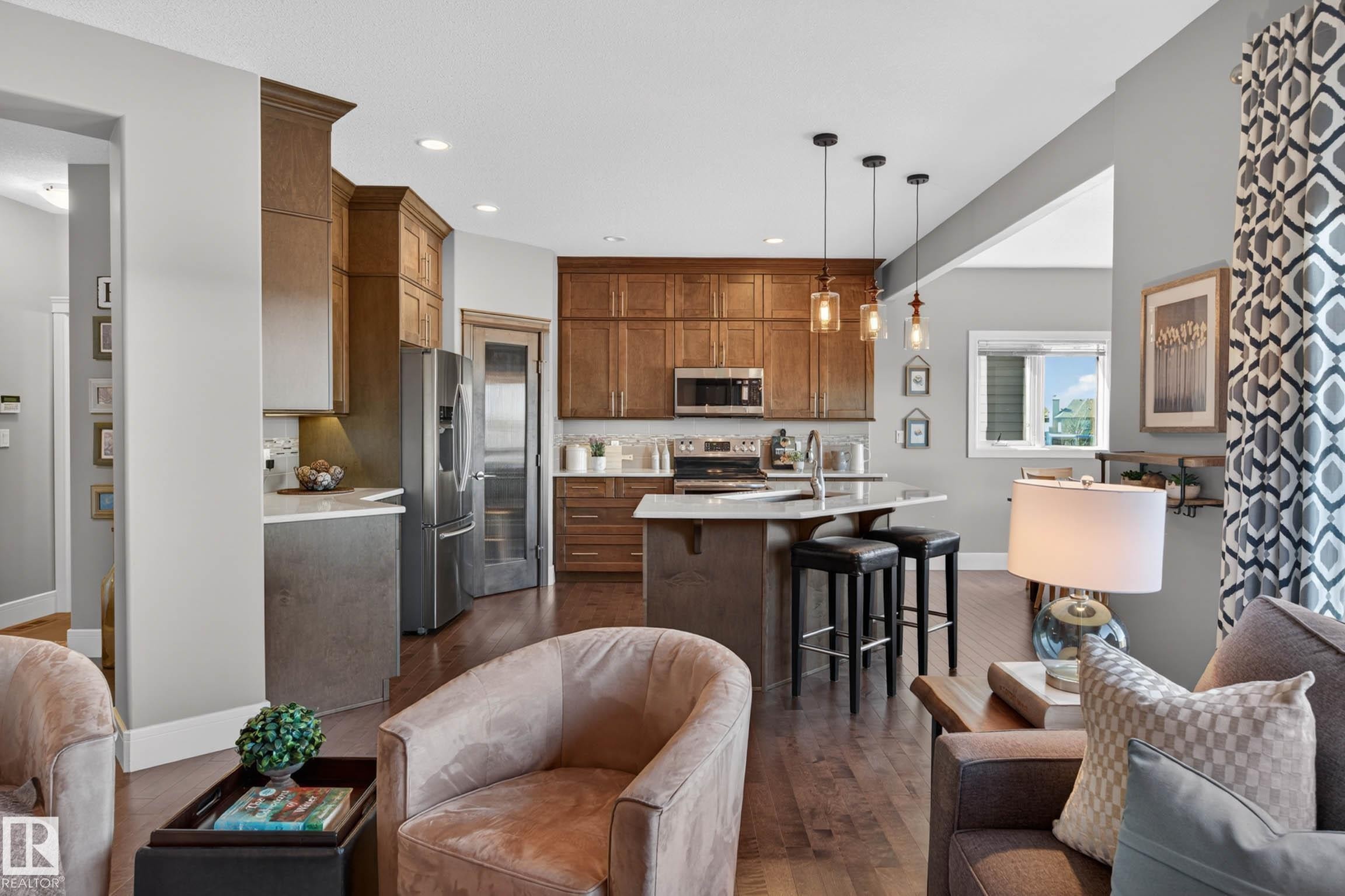 Open-concept kitchen featuring wood-finish flooring, custom cabinetry, stainless steel appliances, a center island with seating, and pendant lighting - 2086 Redtail Common, Edmonton, AB - Indoor
