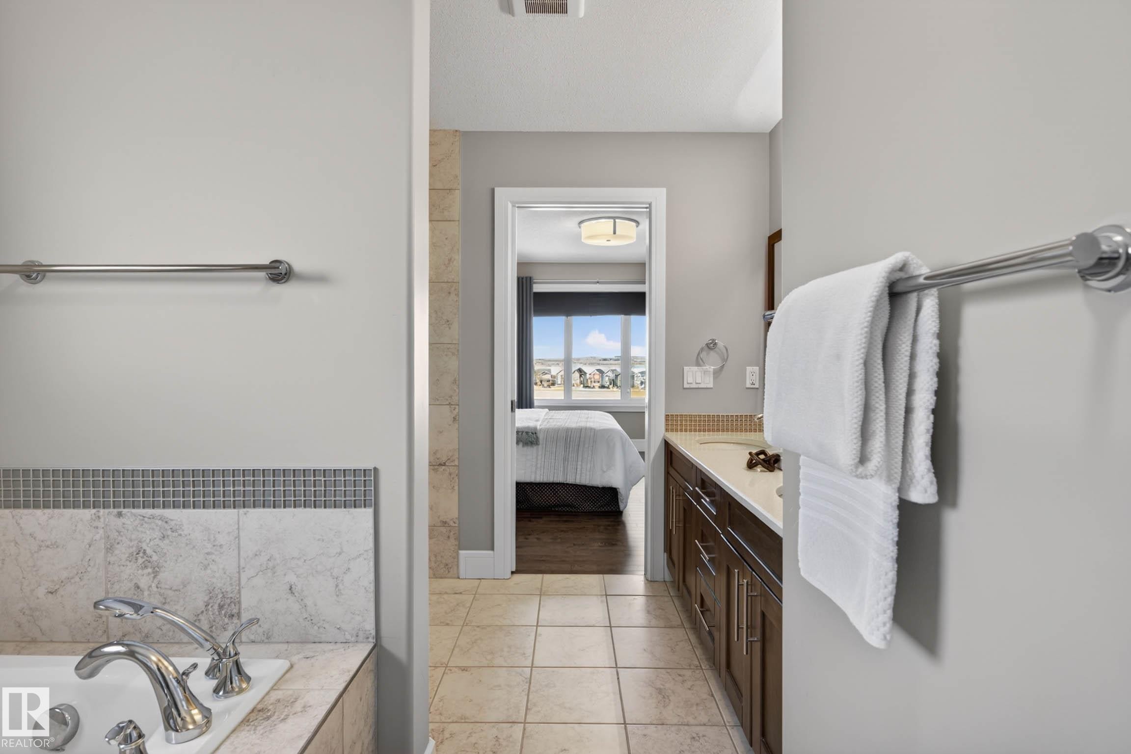 Bathroom featuring a built-in tub with tile surround and chrome fixtures, tile flooring, a dark wood-finish vanity with an undermount sink and light-toned countertop, and modern ceiling lighting - 2086 Redtail Common, Edmonton, AB - Indoor Photo Showing Other Room