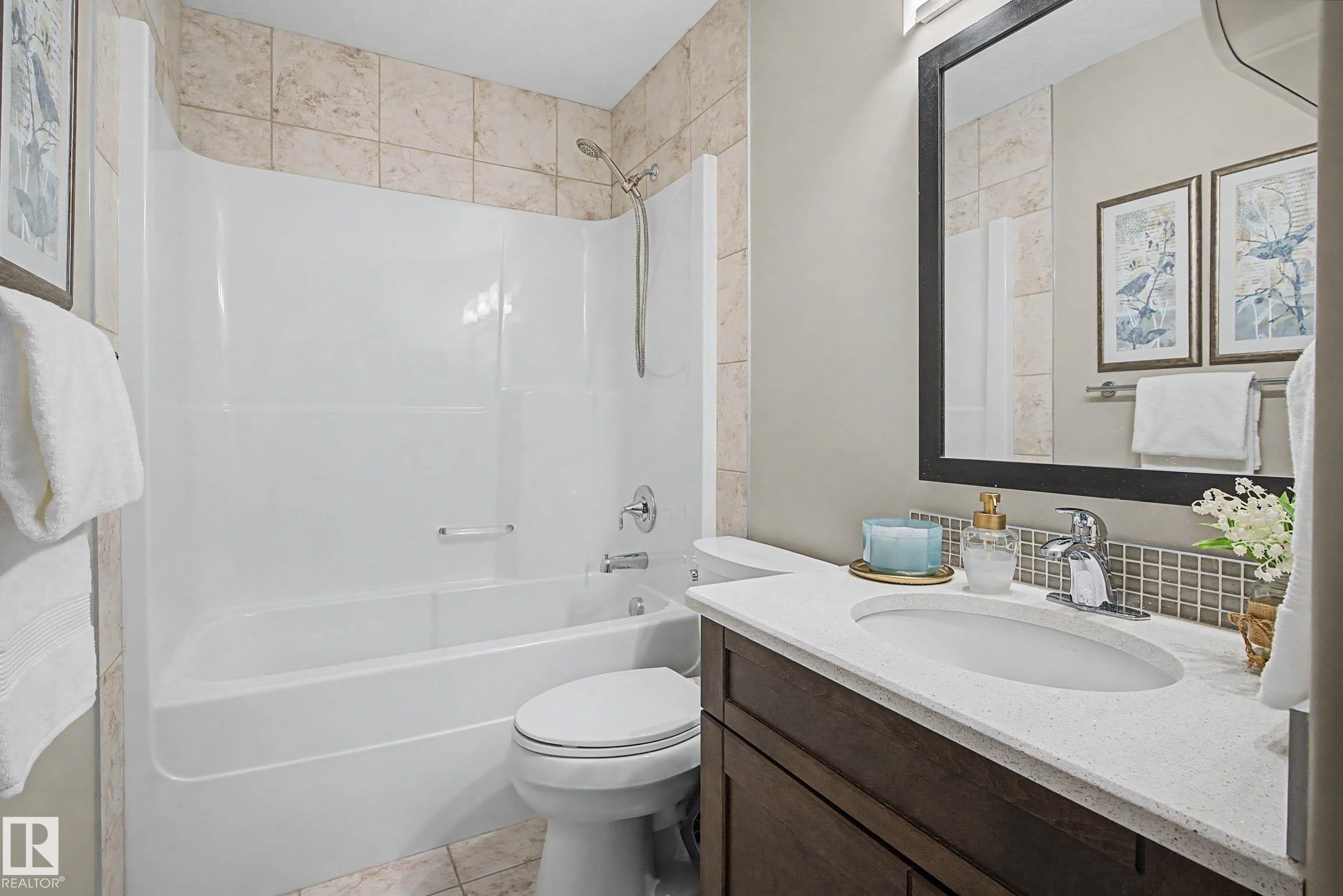 Bathroom featuring a white tub/shower combination, light-toned tile surround, dark wood-finish vanity with an integrated sink, and a light-colored countertop - 2086 Redtail Common, Edmonton, AB - Indoor Photo Showing Bathroom