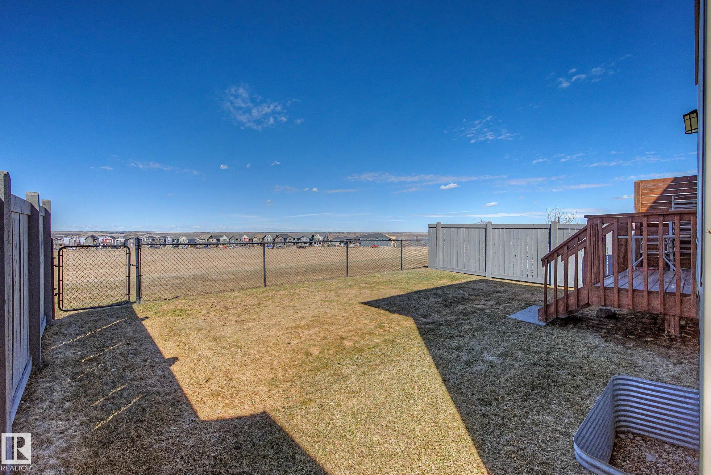 Expansive backyard featuring a brown wooden deck with stairs, a chain-link fence with a gate, and privacy fencing - 2086 Redtail Common, Edmonton, AB - Outdoor