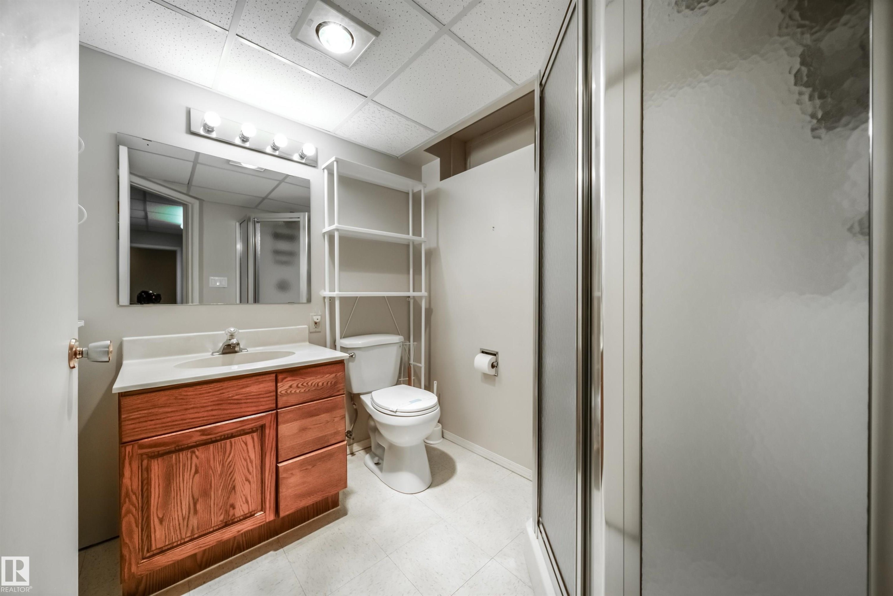 Bathroom featuring a wood-finish vanity with a light-colored countertop, an attached mirror, a built-in shower enclosure with frosted panels, and recessed ceiling lighting - 10231 46 Street, Edmonton, AB - Indoor Photo Showing Bathroom