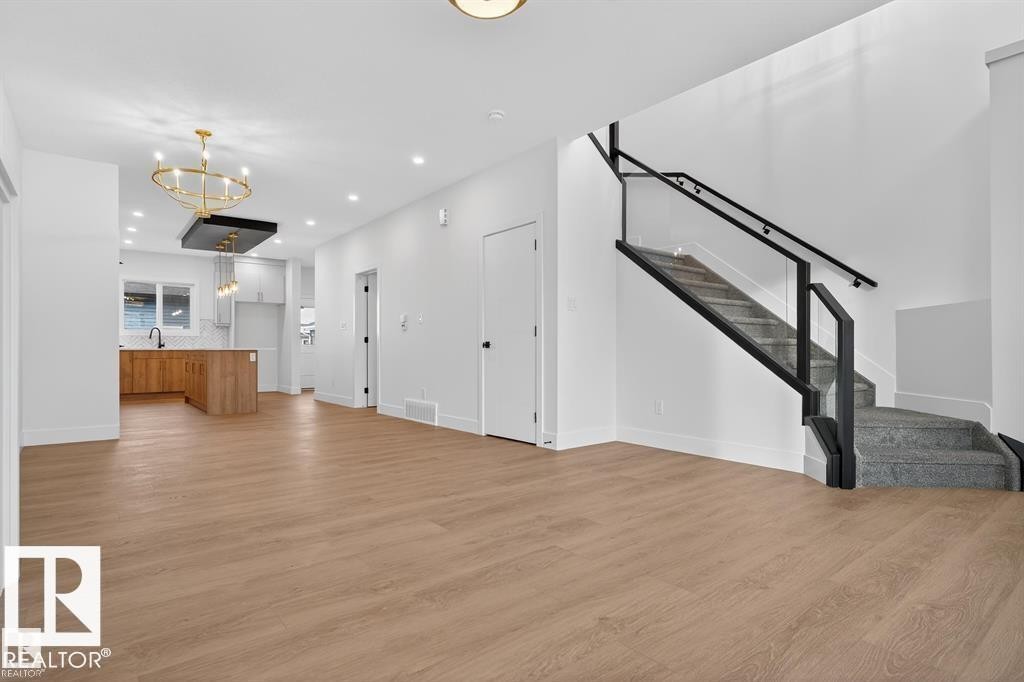 Open concept living space featuring wood-finish flooring, a modern staircase with glass railing and black handrails, recessed lighting, and a contemporary gold chandelier - 55 Rosa Crescent, St. Albert, AB - Indoor Photo Showing Other Room