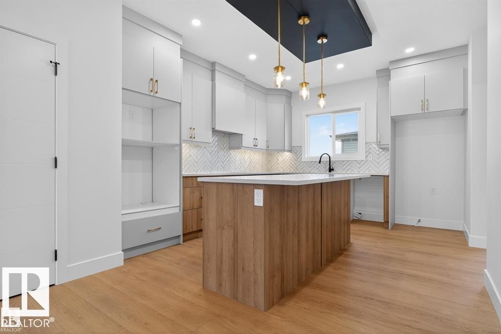 Modern kitchen featuring a central island with wood-finish paneling, white countertop, and gold-toned pendant lighting - 55 Rosa Crescent, St. Albert, AB - Indoor Photo Showing Kitchen