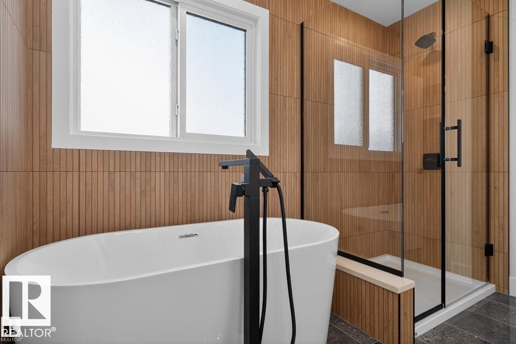 Freestanding soaking tub with a matte black floor-mounted faucet, glass-enclosed shower with a rainfall showerhead, and wood-finish vertical paneling - 55 Rosa Crescent, St. Albert, AB - Indoor