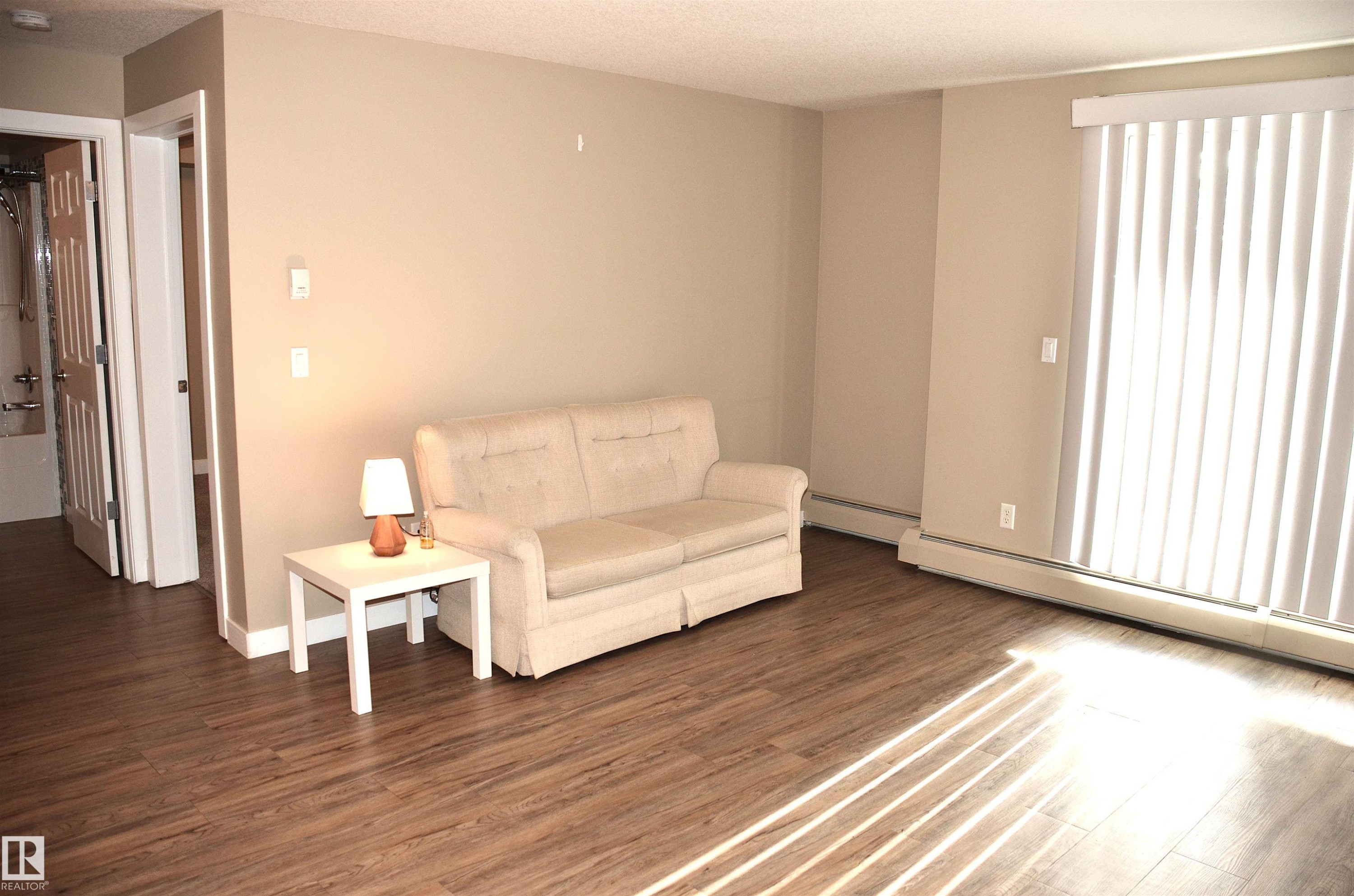 Living area featuring wood-finish flooring, neutral wall tones, and vertical blinds on the sliding glass door - 103 920 156 Street Nw, Edmonton, AB - Indoor Photo Showing Other Room