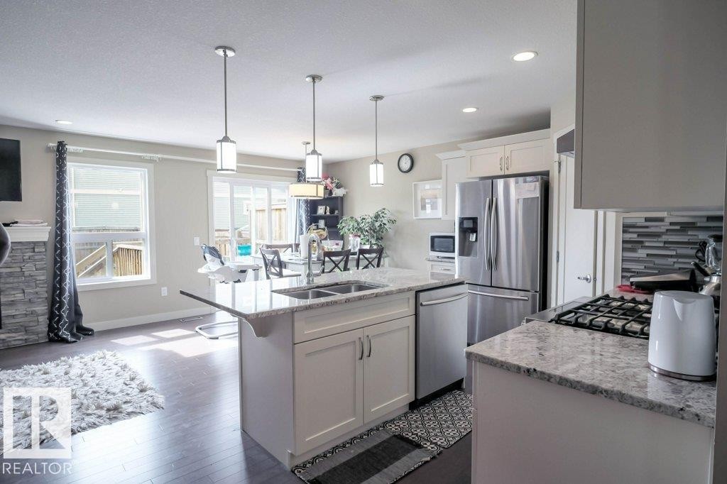 Kitchen featuring an island with double sinks, stainless steel appliances, white cabinetry, granite countertops, and wood-finish flooring - 16619 14 Avenue, Edmonton, AB - Indoor Photo Showing Kitchen With Stainless Steel Kitchen With Double Sink With Upgraded Kitchen
