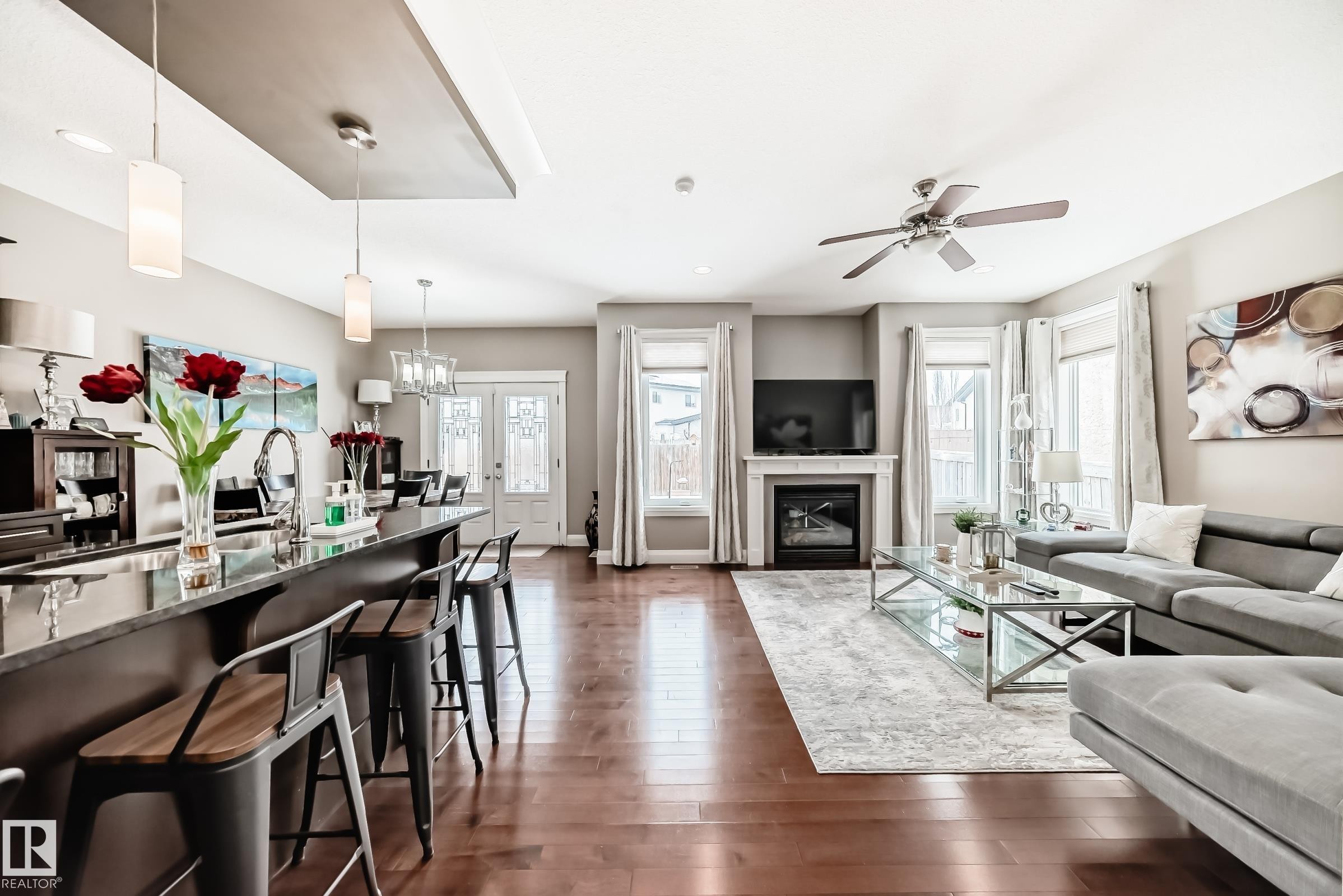 This open-concept interior features rich hardwood flooring, a kitchen island with seating, a fireplace with a mantel, and large windows that provide natural light - 3220 151 Avenue, Edmonton, AB - Indoor Photo Showing Living Room With Fireplace