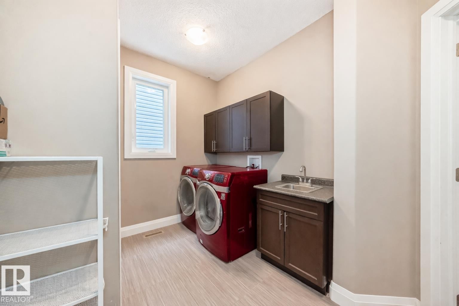 The property features a dedicated laundry area with a window, dark cabinetry, and a utility sink set in a countertop - 3220 151 Avenue, Edmonton, AB - Indoor Photo Showing Laundry Room