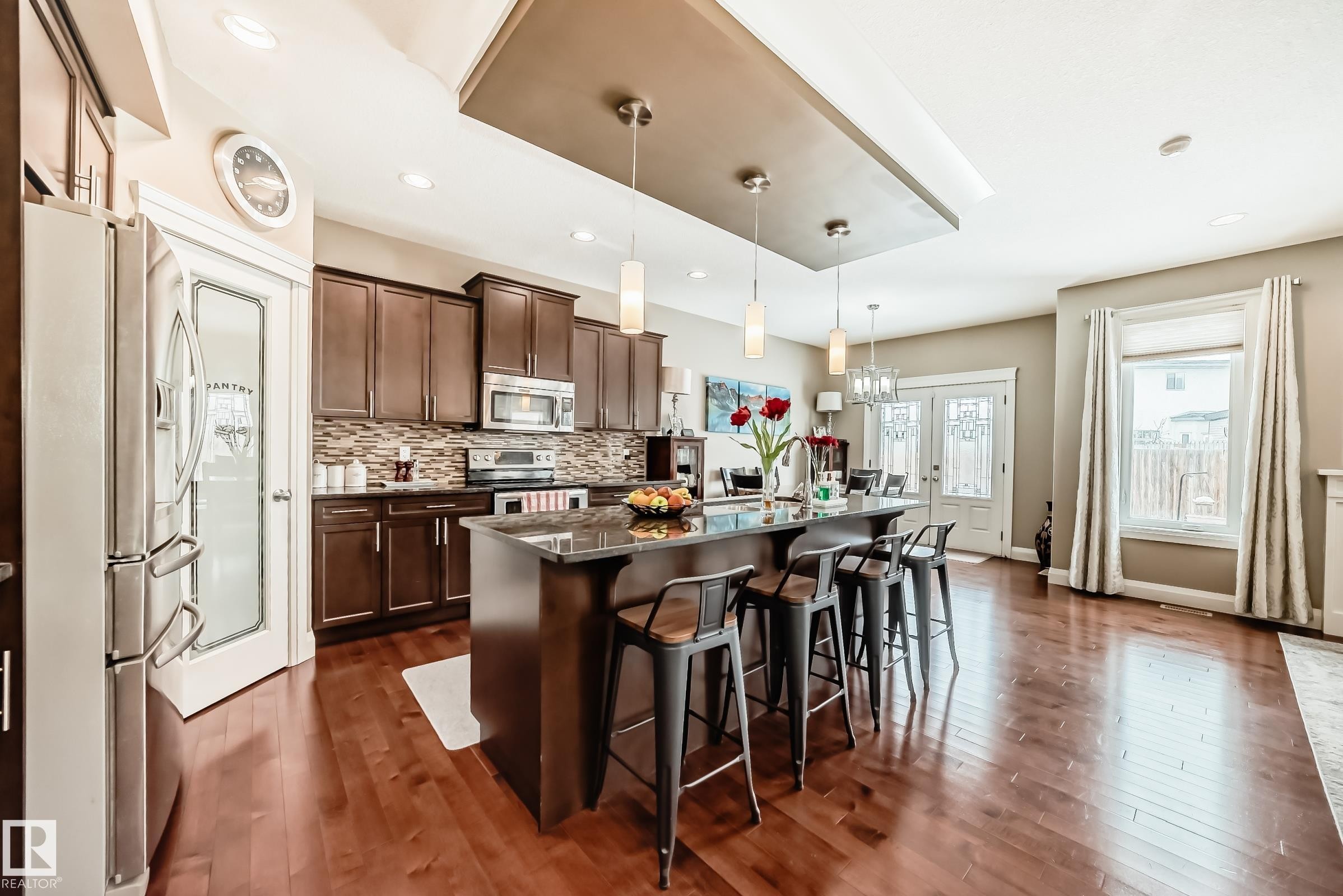 This bright kitchen features hardwood flooring, dark wood cabinetry, and stainless steel appliances - 3220 151 Avenue, Edmonton, AB - Indoor Photo Showing Kitchen With Upgraded Kitchen