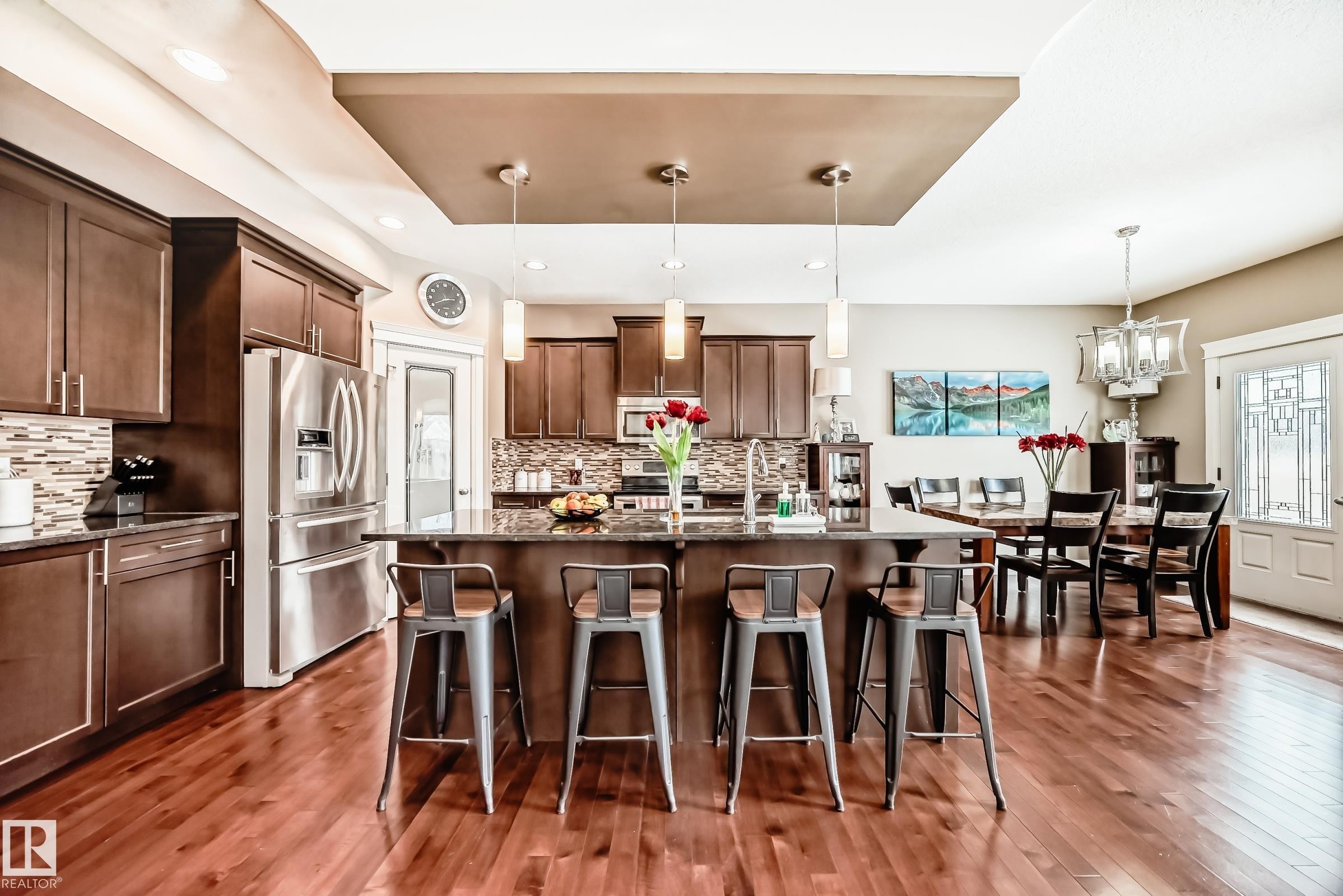 The kitchen features rich hardwood flooring, dark wood cabinetry, a large kitchen island with pendant lighting, and stainless steel appliances - 3220 151 Avenue, Edmonton, AB - Indoor