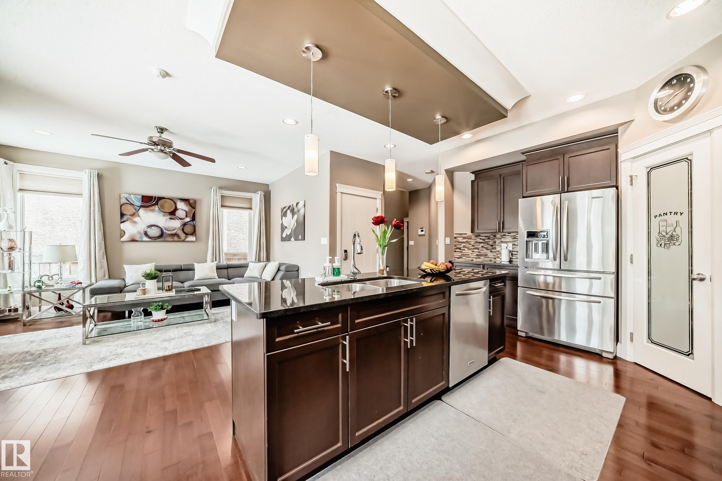 Open concept living area featuring dark hardwood floors, a kitchen island with pendant lighting, stainless steel appliances, and a pantry with a frosted glass door - 3220 151 Avenue, Edmonton, AB - Indoor Photo Showing Kitchen With Stainless Steel Kitchen With Upgraded Kitchen