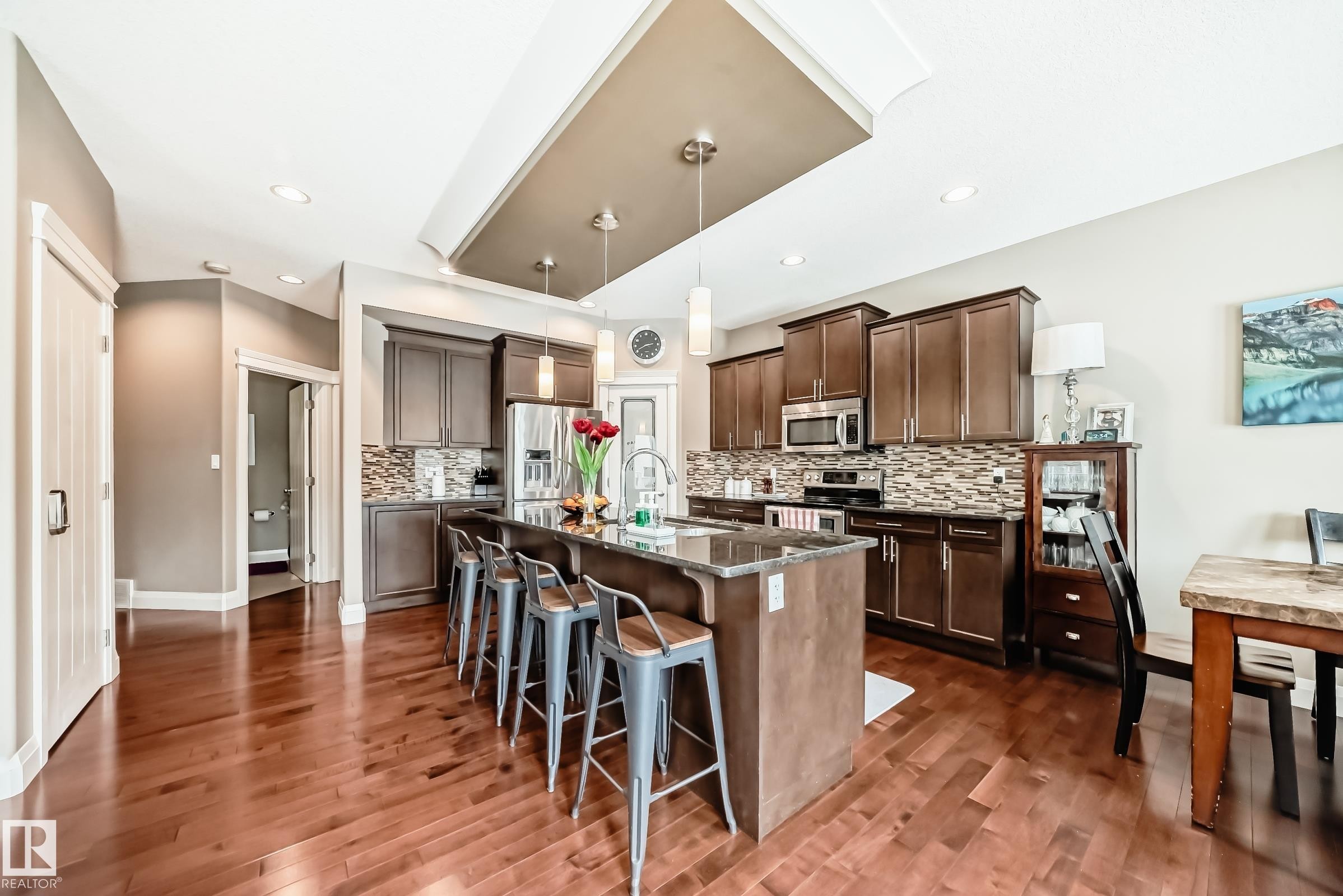 The kitchen features rich wood flooring, dark wood cabinetry, stainless steel appliances, and an island with a breakfast bar - 3220 151 Avenue, Edmonton, AB - Indoor