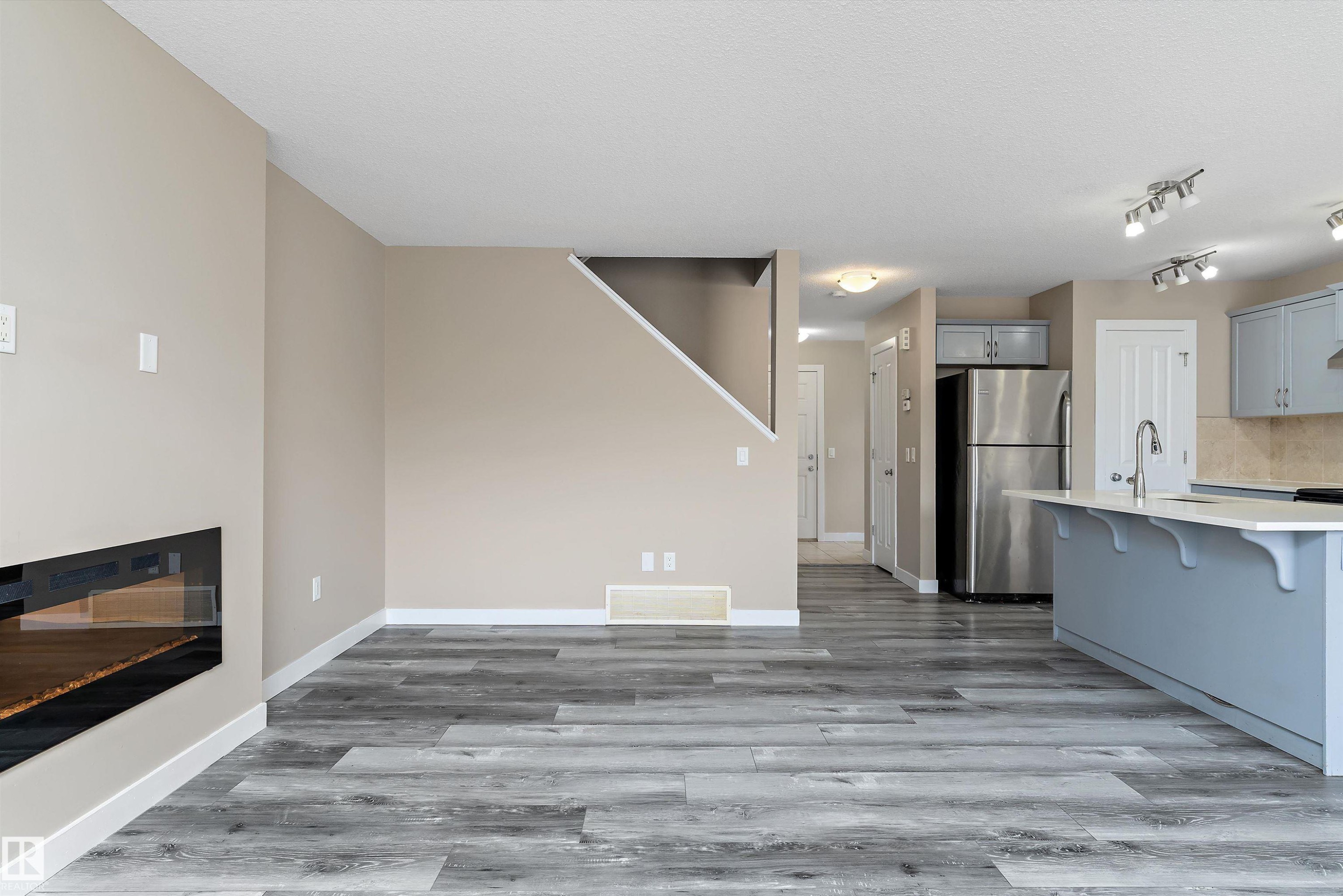 Open-concept living space featuring wood-finish flooring, a modern linear fireplace, a kitchen island with seating, stainless steel appliances, and track lighting - 3314 9 Street Nw, Edmonton, AB - Indoor Photo Showing Kitchen