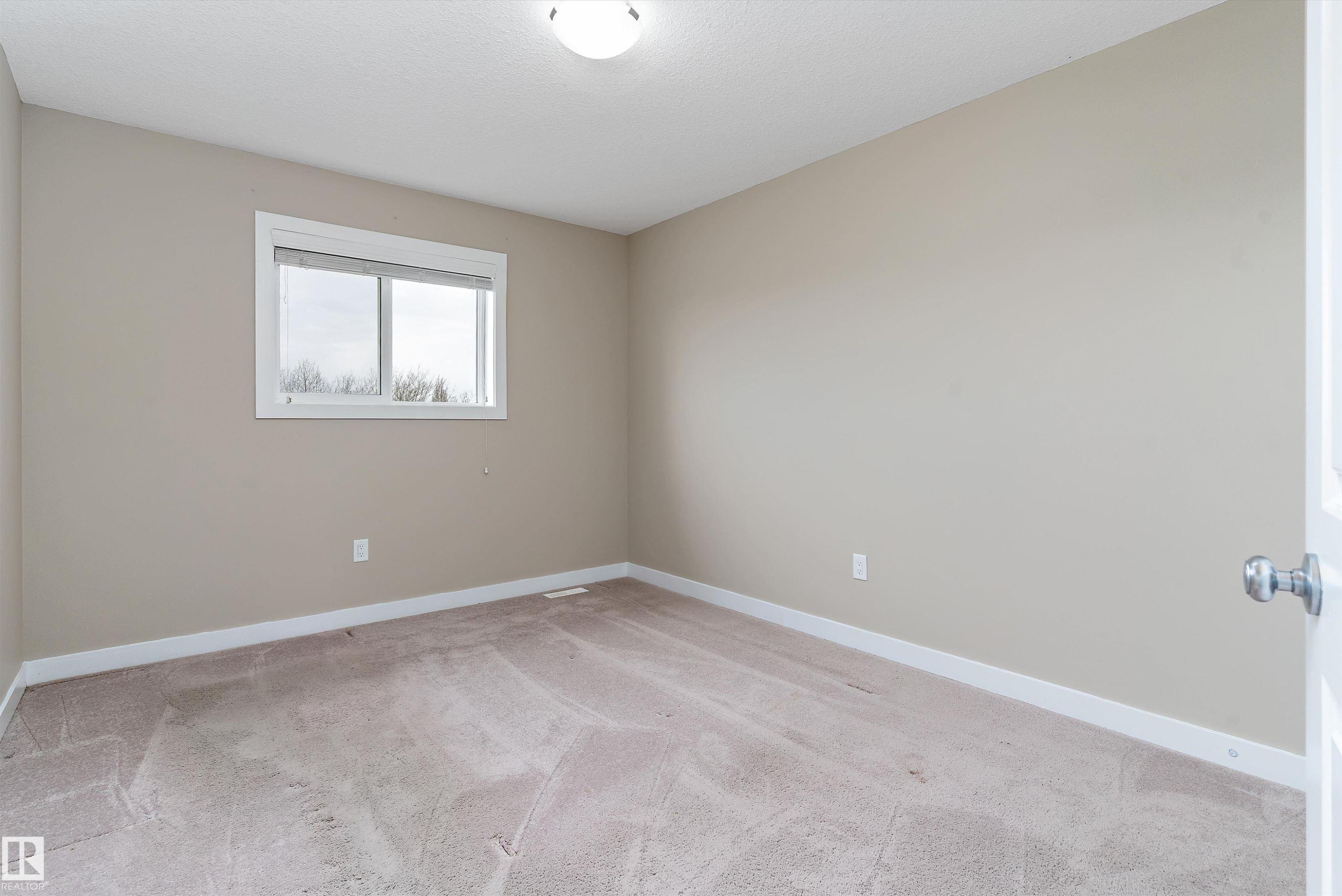 Neutral-toned room with a large window, light brown carpet, white baseboards, and a flush mount ceiling light fixture - 3314 9 Street Nw, Edmonton, AB - Indoor Photo Showing Other Room