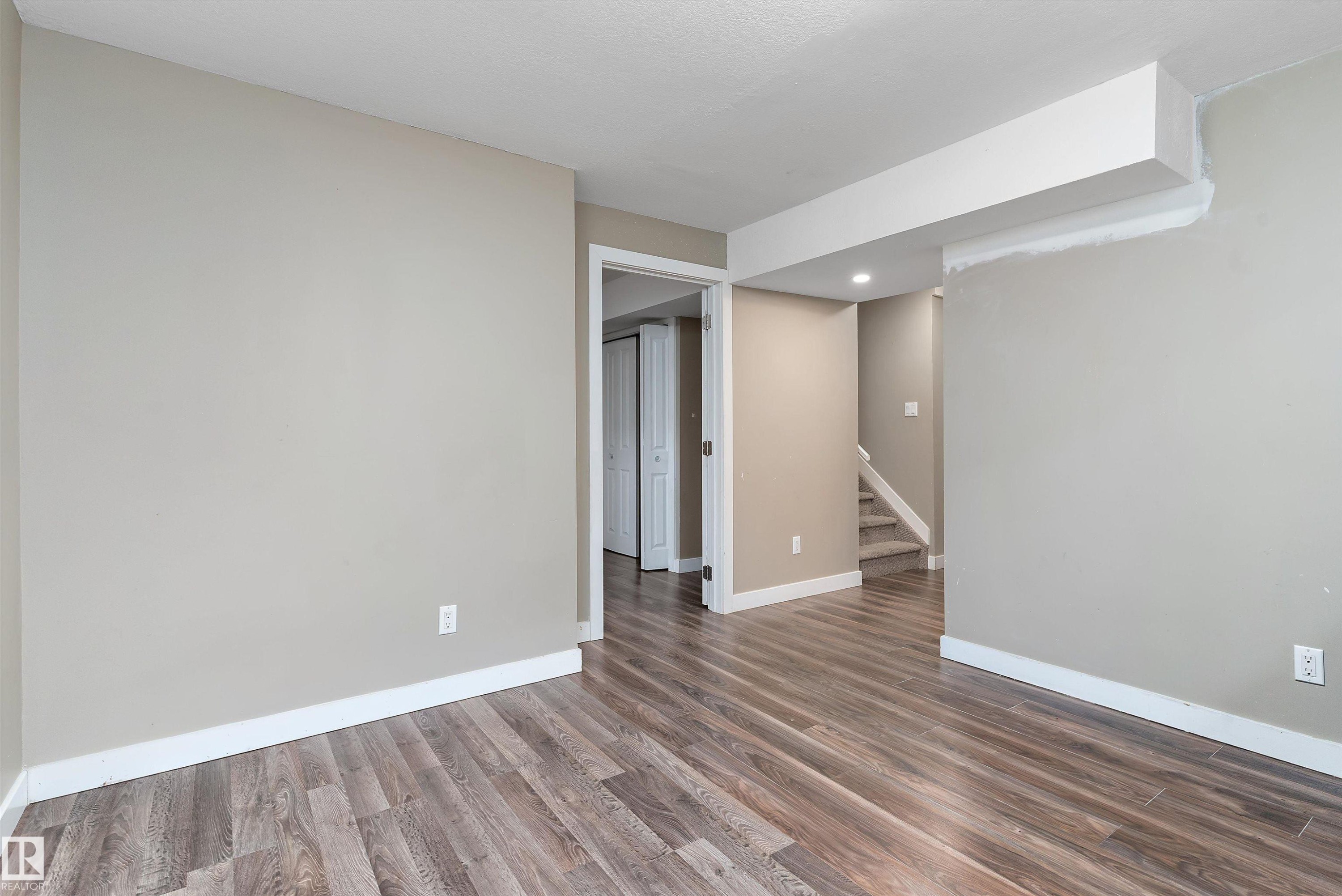 Spacious interior room featuring wood-finish flooring, neutral wall paint, white trim, recessed lighting, and a visible doorway leading to an additional space - 3314 9 Street Nw, Edmonton, AB - Indoor Photo Showing Other Room
