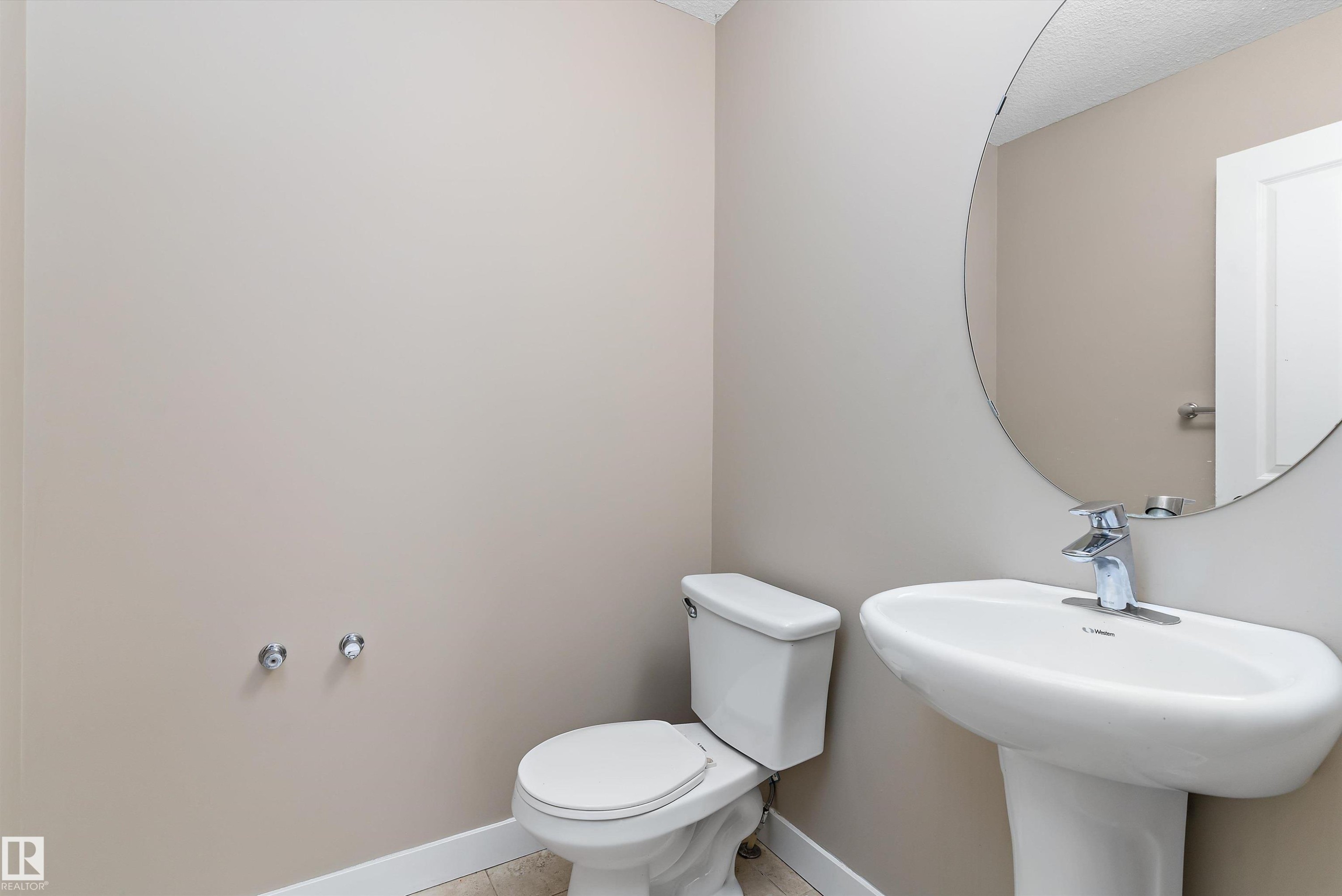 Pedestal sink with chrome faucet, circular wall mirror, and neutral painted walls - 3314 9 Street Nw, Edmonton, AB - Indoor Photo Showing Bathroom