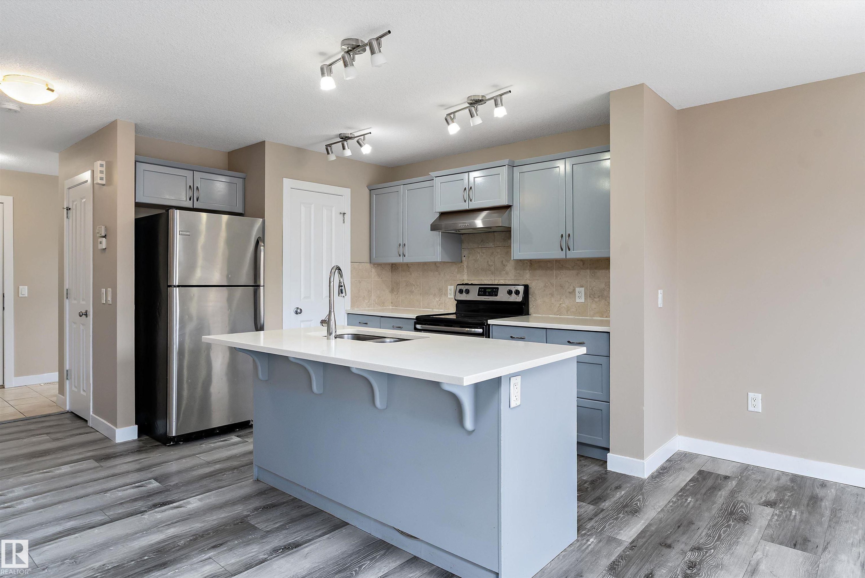Modern kitchen featuring a central island with a white countertop and integrated sink, stainless steel refrigerator, black range, and blue cabinetry - 3314 9 Street Nw, Edmonton, AB - Indoor Photo Showing Kitchen With Upgraded Kitchen