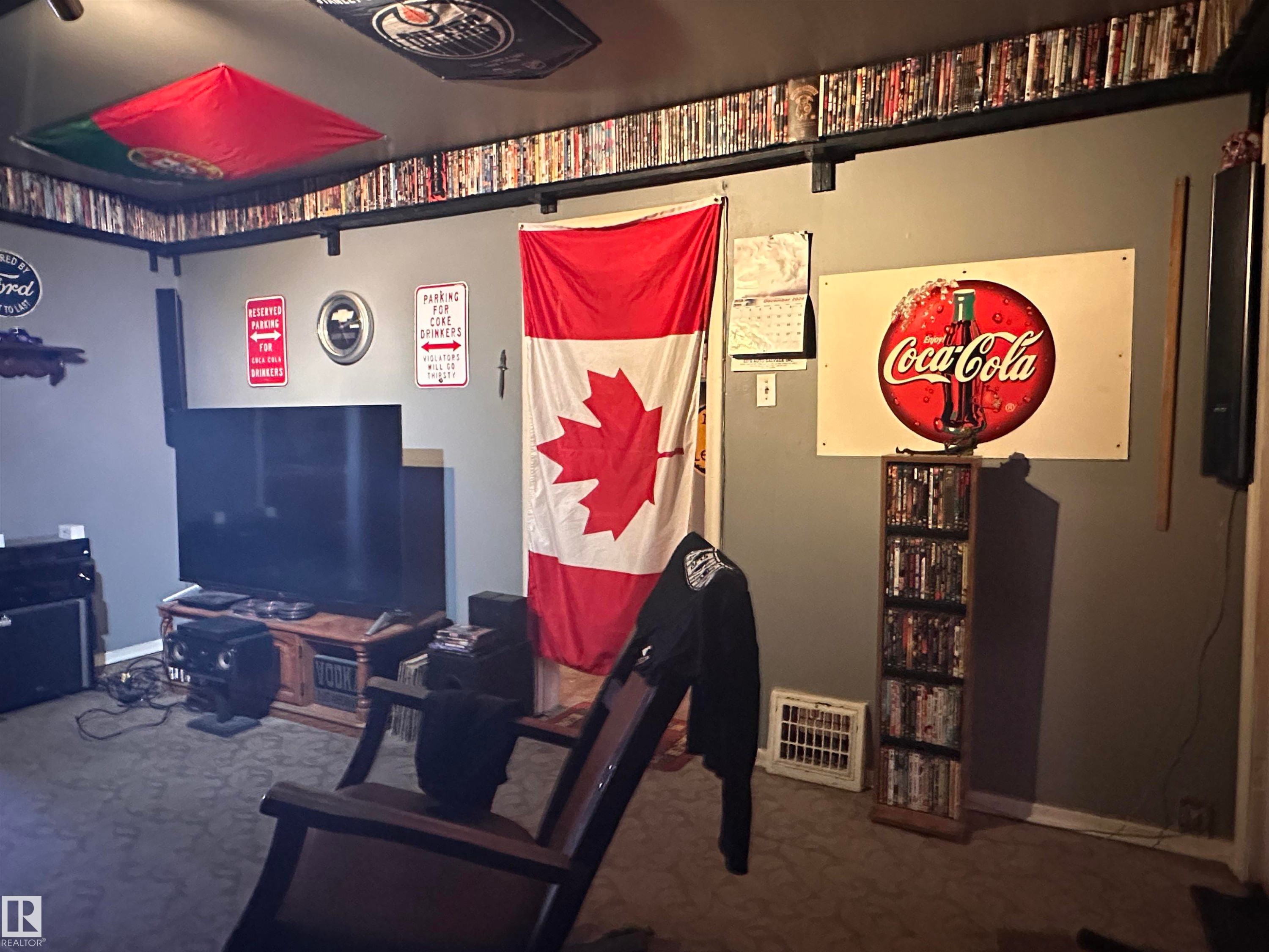 Carpeted room featuring a media console with a television, a built-in shelf above, and a wall-mounted Coca-Cola sign - 10528 100 Avenue, Westlock, AB - Indoor Photo Showing Other Room
