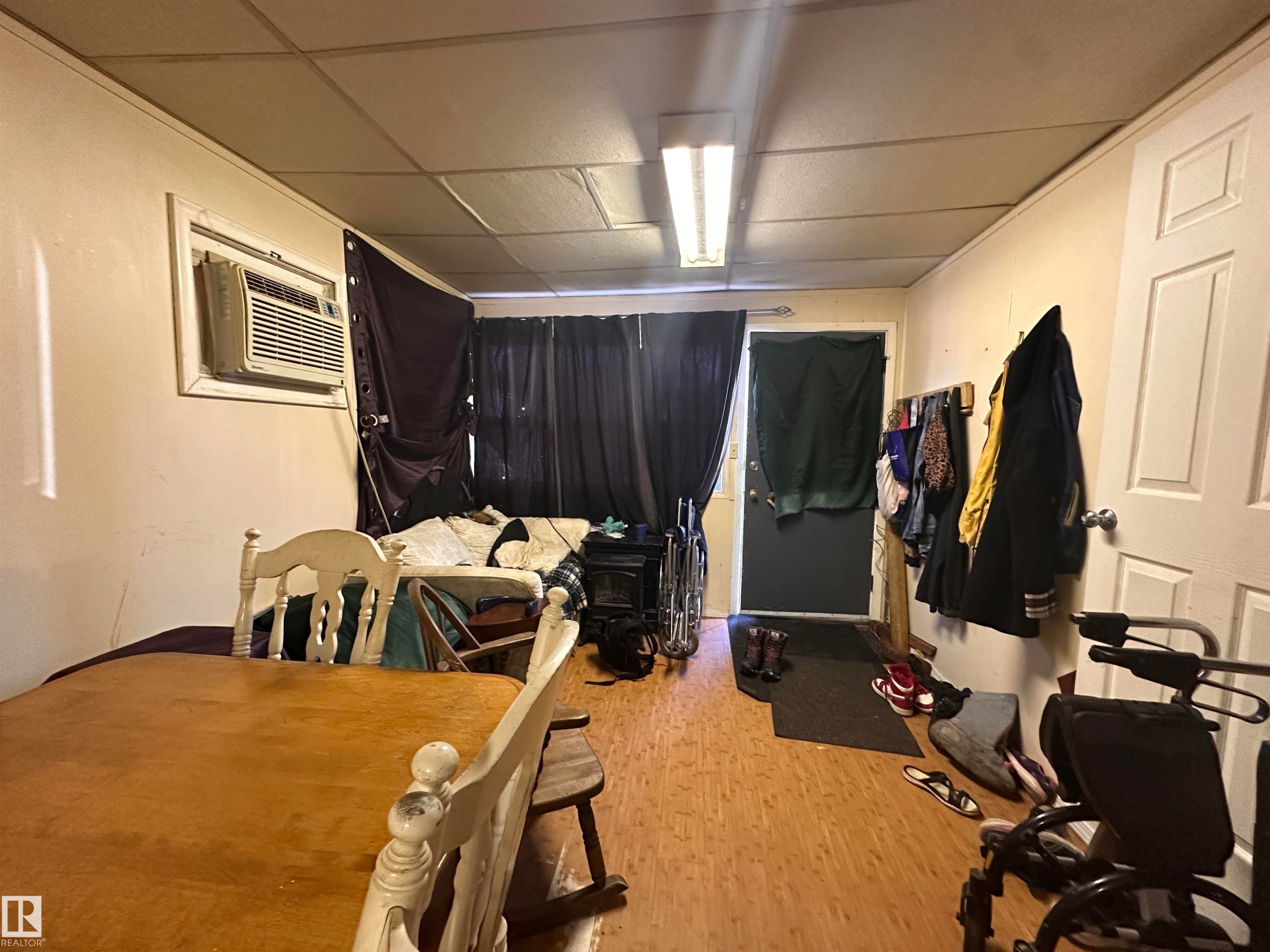 Room featuring wood-finish flooring, a wall-mounted air conditioning unit, and a drop ceiling - 10528 100 Avenue, Westlock, AB - Indoor