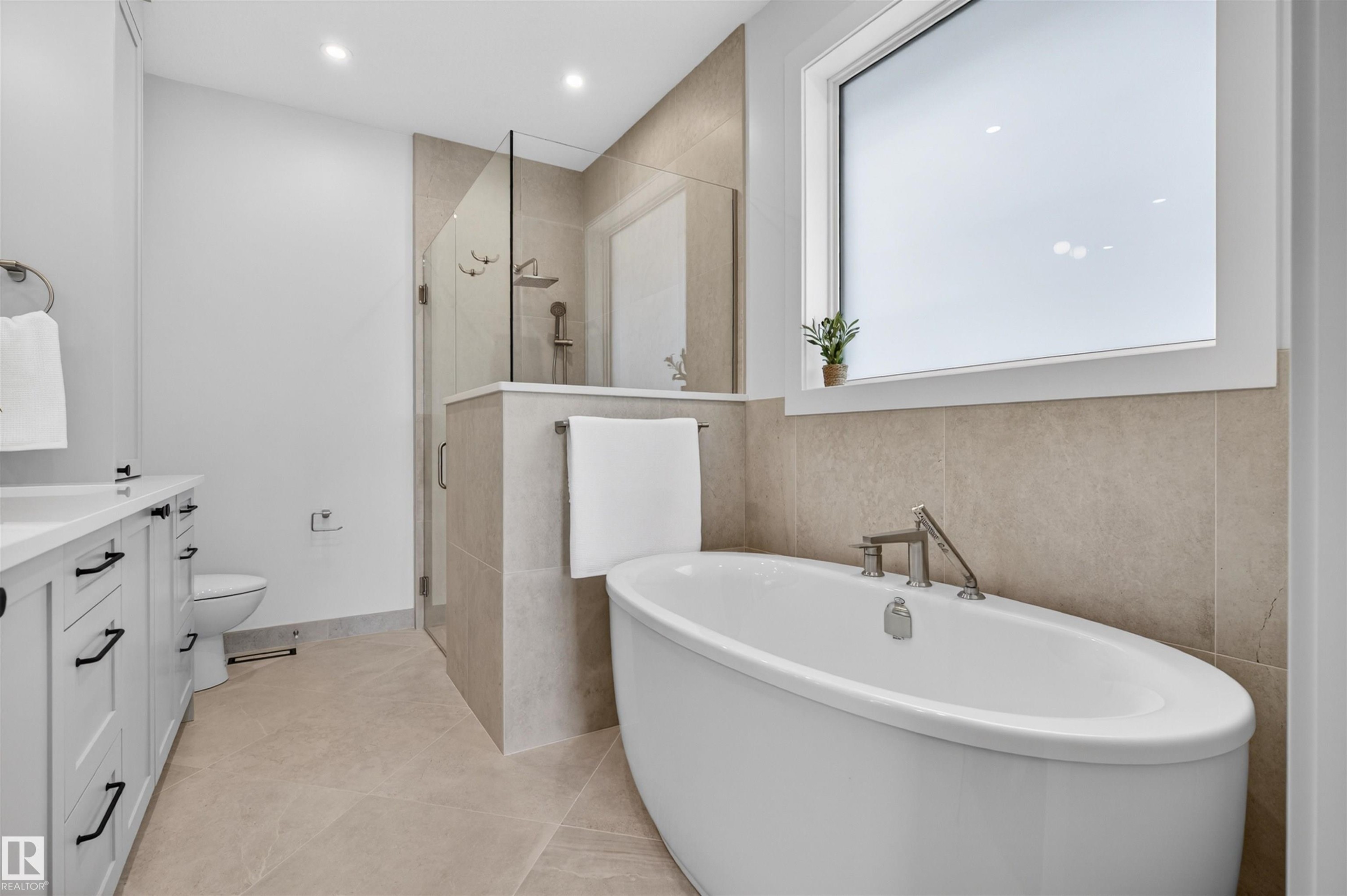 Freestanding soaking tub with chrome fixtures, an adjacent glass-enclosed shower, and a double vanity with white cabinetry and dark hardware - 149 Eastgate Way, St. Albert, AB - Indoor Photo Showing Bathroom