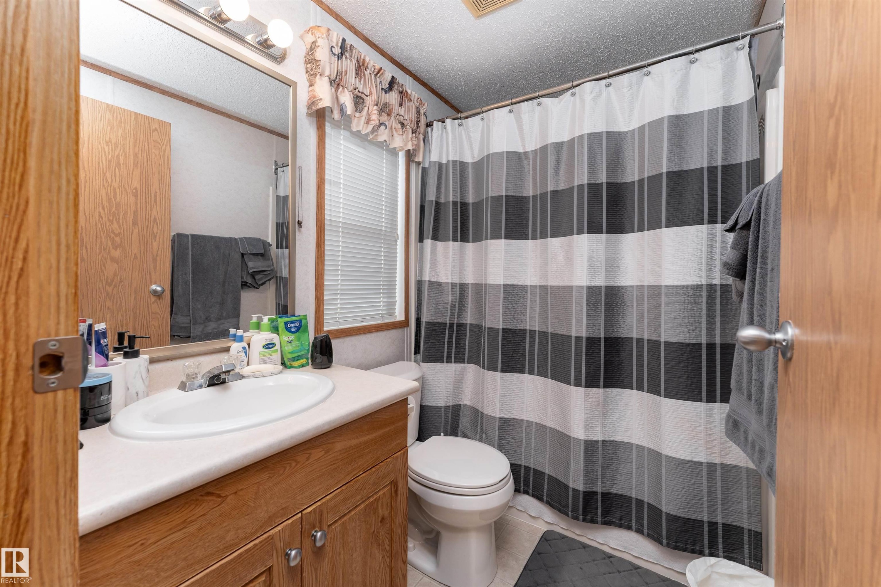The bathroom features a vanity with wooden cabinetry, a white countertop, and a mirror with overhead lighting - 1663 Jubilee Crescent, Sherwood Park, AB - Indoor Photo Showing Bathroom