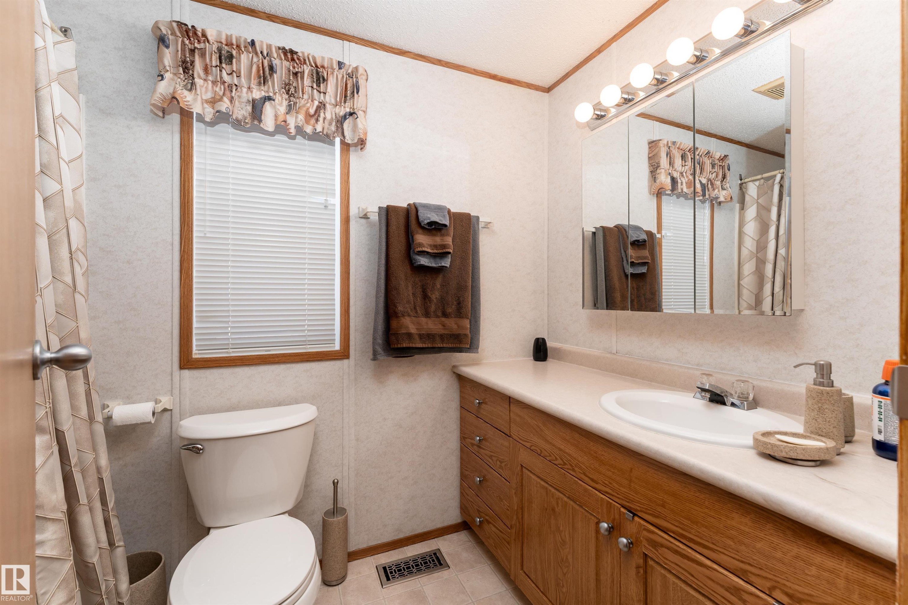 The bathroom features a wooden vanity with a sink, a wall-mounted mirror with integrated lighting, and a window with blinds - 1663 Jubilee Crescent, Sherwood Park, AB - Indoor Photo Showing Bathroom