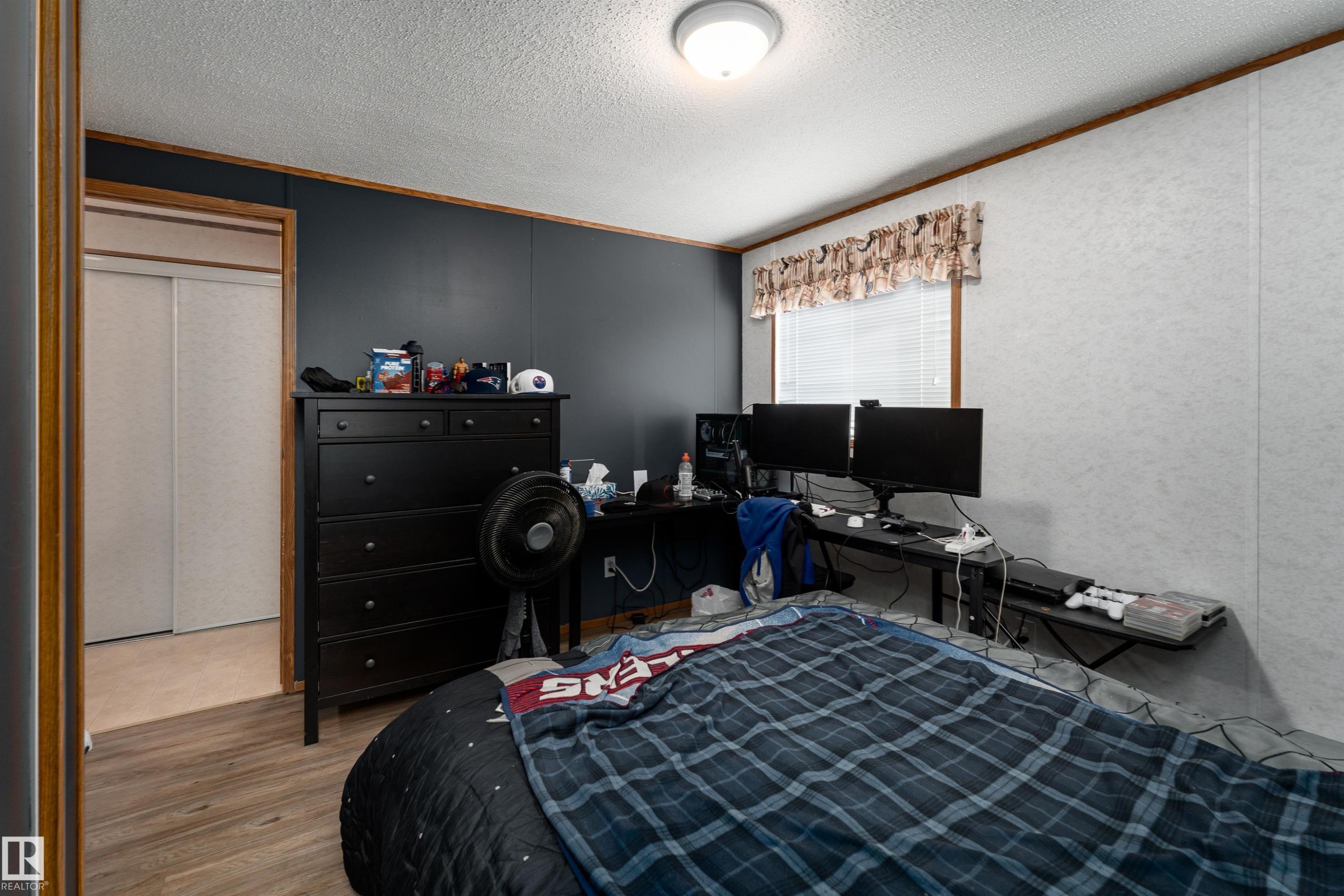This room features a window with blinds and a patterned valance, wood-look flooring, and a ceiling-mounted light fixture - 1663 Jubilee Crescent, Sherwood Park, AB - Indoor Photo Showing Bedroom