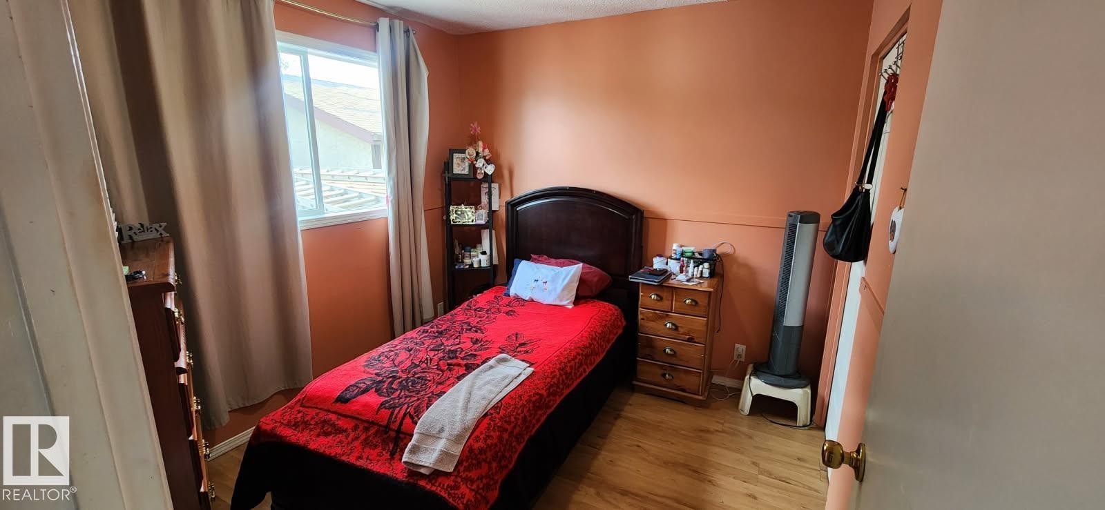 Room featuring wood-finish flooring, a window with curtains, and a painted accent wall - 14411 31 Street, Edmonton, AB - Indoor Photo Showing Bedroom