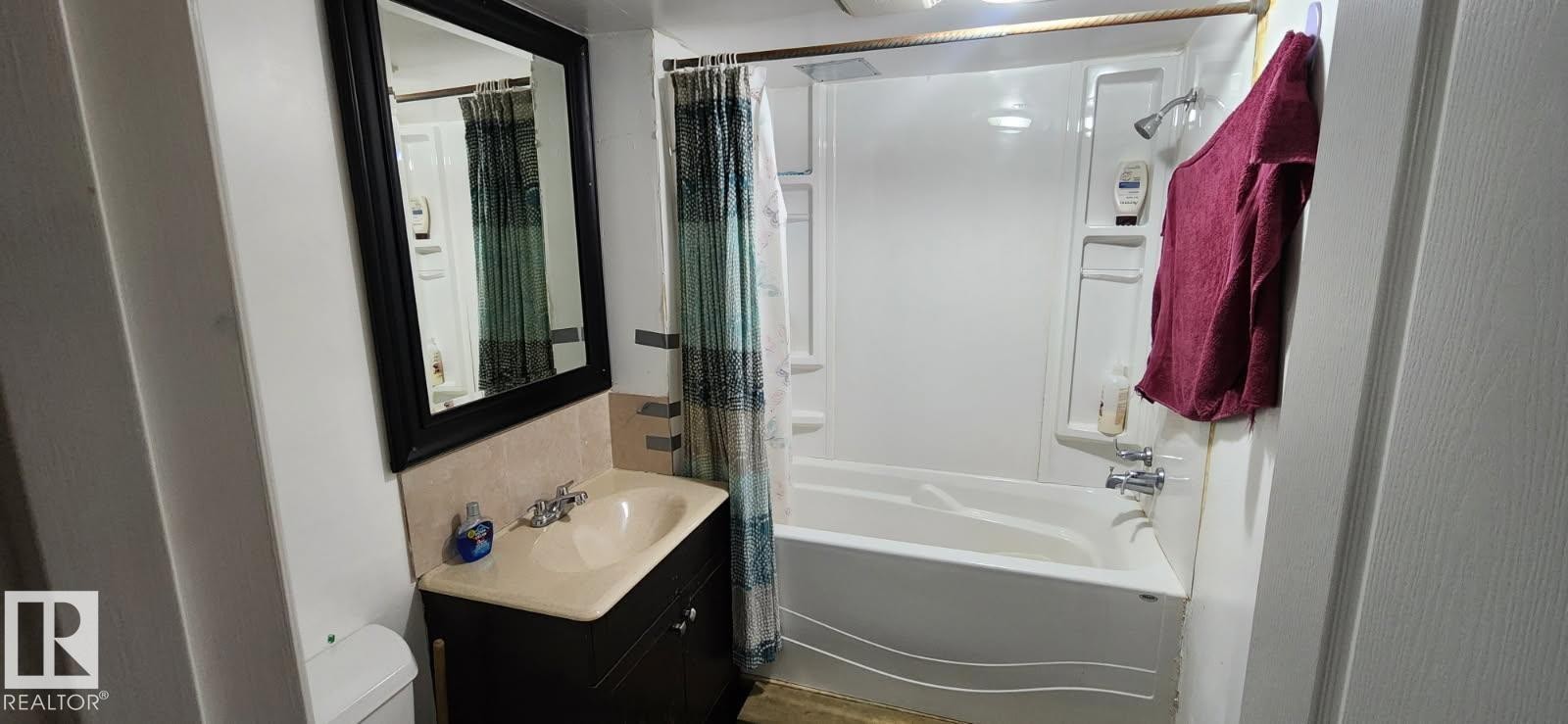 Bathroom featuring a dark wood-finish vanity with an integrated sink, a framed mirror, and a full bathtub with a shower fixture - 14411 31 Street, Edmonton, AB - Indoor Photo Showing Bathroom