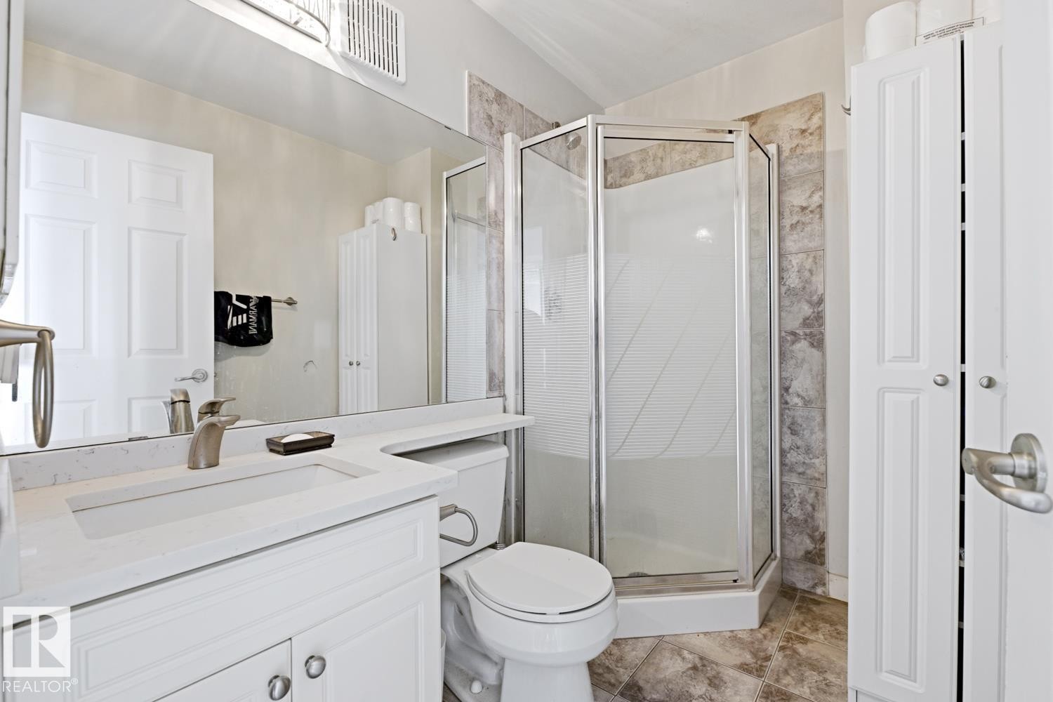 Bathroom featuring a corner shower enclosure, white vanity with integrated sink, a commode, a large wall-mounted mirror, and tile flooring - #115 10105 95 St Nw, Edmonton, AB - Indoor Photo Showing Bathroom