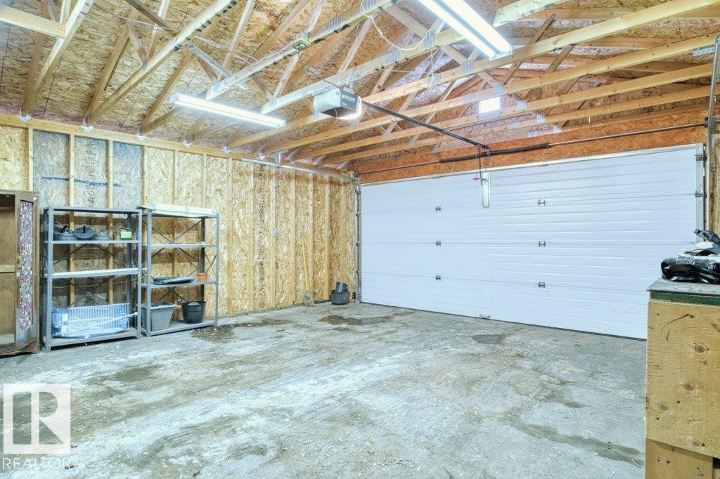 Interior garage space featuring an overhead sectional door, exposed wood rafters, fluorescent lighting, and concrete flooring - 12207 110 Avenue, Edmonton, AB - Indoor Photo Showing Garage