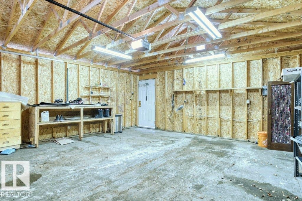 Spacious garage featuring exposed wood framing, ample overhead lighting, a built-in workbench, and a dedicated utility area - 12207 110 Avenue, Edmonton, AB - Indoor