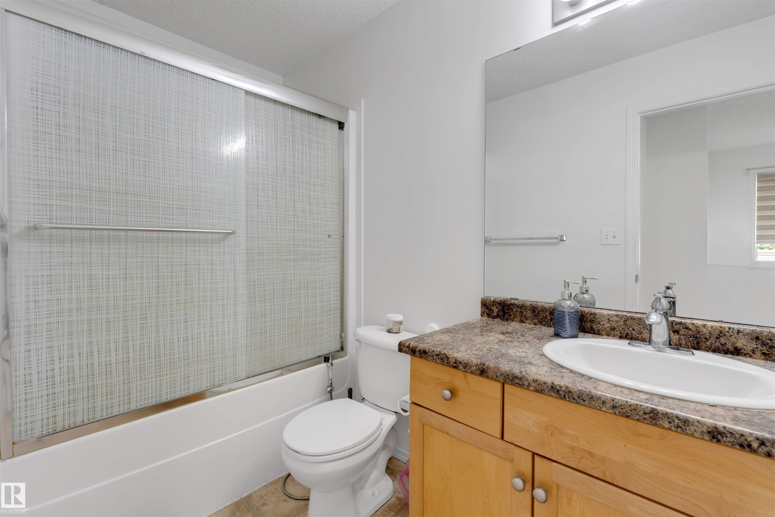 Bathroom featuring a tub and shower combination with sliding textured glass doors, a vanity with wood-finish cabinetry, a white oval sink, and a speckled countertop - 48 2503 24 Street, Edmonton, AB - Indoor Photo Showing Bathroom