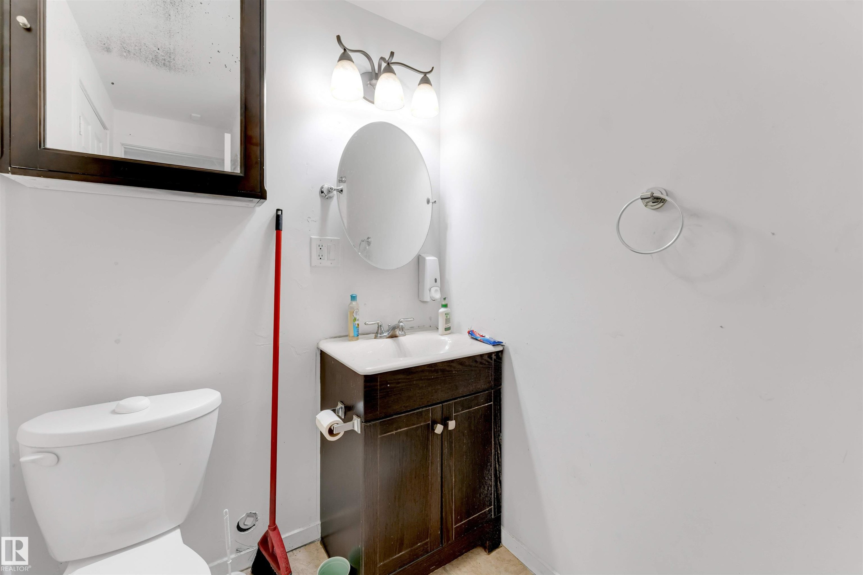 Modern bathroom featuring a white toilet, a dark wood-finish vanity with a white sink, an oval mirror, and a three-light vanity fixture - 48 2503 24 Street, Edmonton, AB - Indoor Photo Showing Bathroom