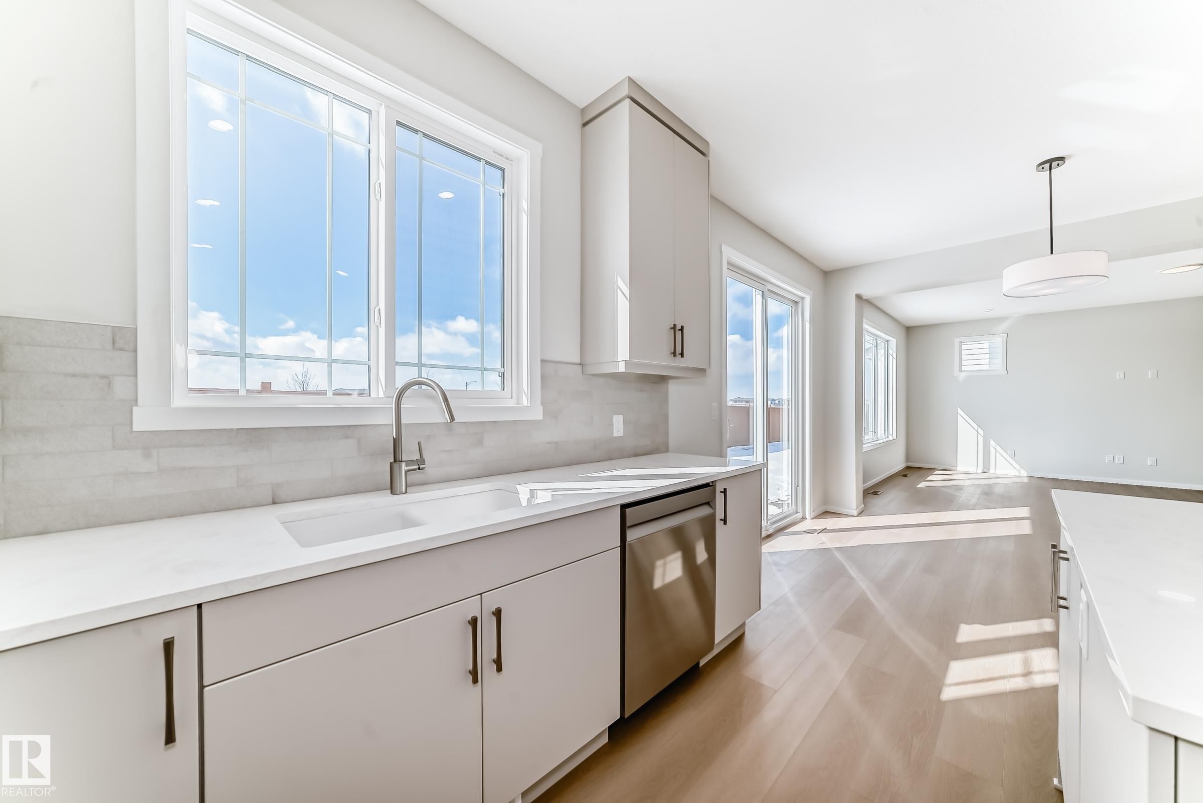 The kitchen features light-colored cabinetry with dark hardware, a stainless steel dishwasher, and a window above the sink - 1516 206 Street Nw, Edmonton, AB - Indoor Photo Showing Kitchen